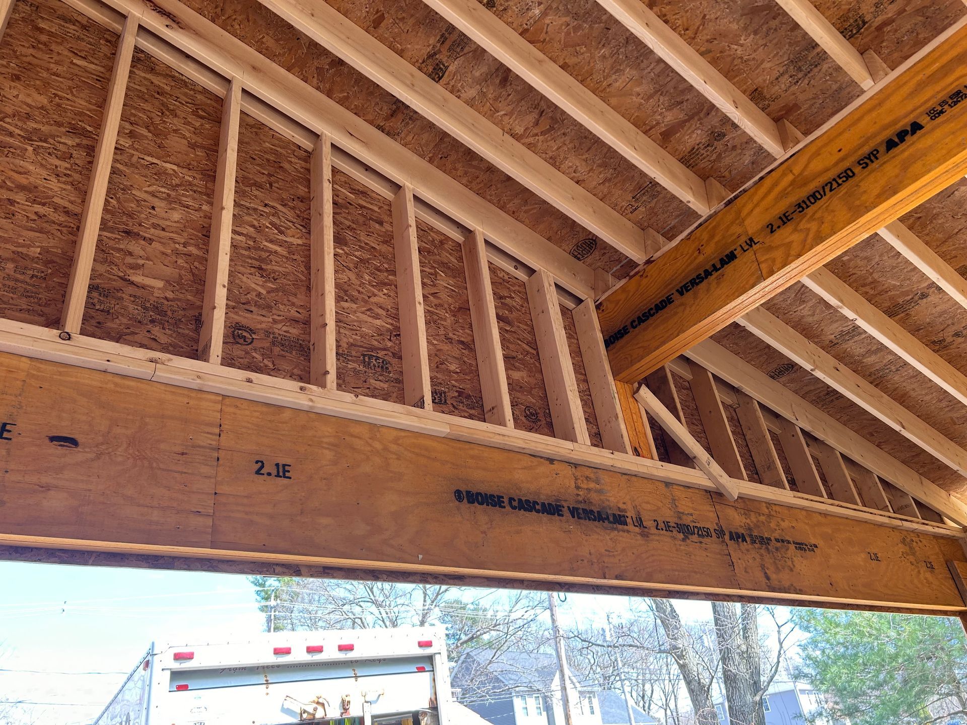 Wooden frame construction of a roof, seen from below, with beams, rafters, and a visible support structure, likely an outdoor area.