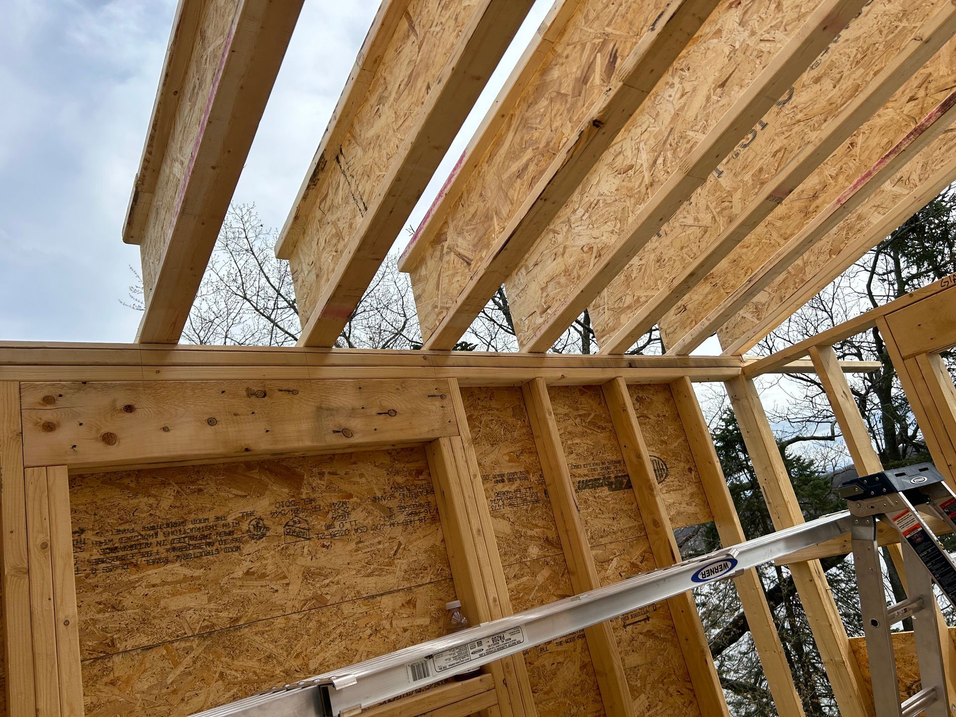 Wooden house frame under construction, with exposed beams and oriented strand board (OSB) panels.