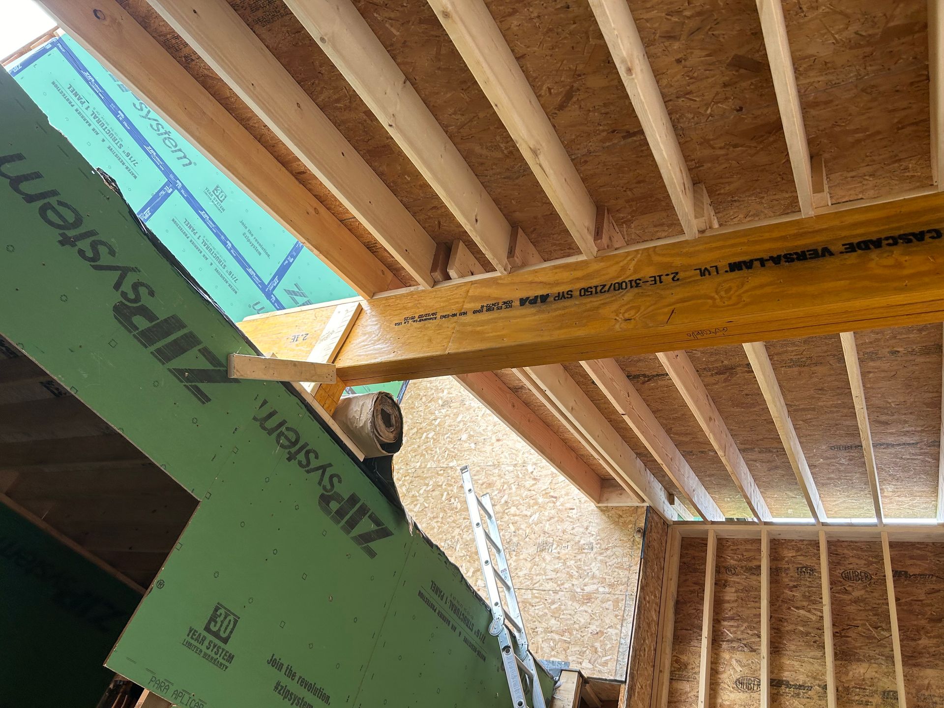 Construction of a building's roof and walls, with exposed wooden beams and green sheathing.
