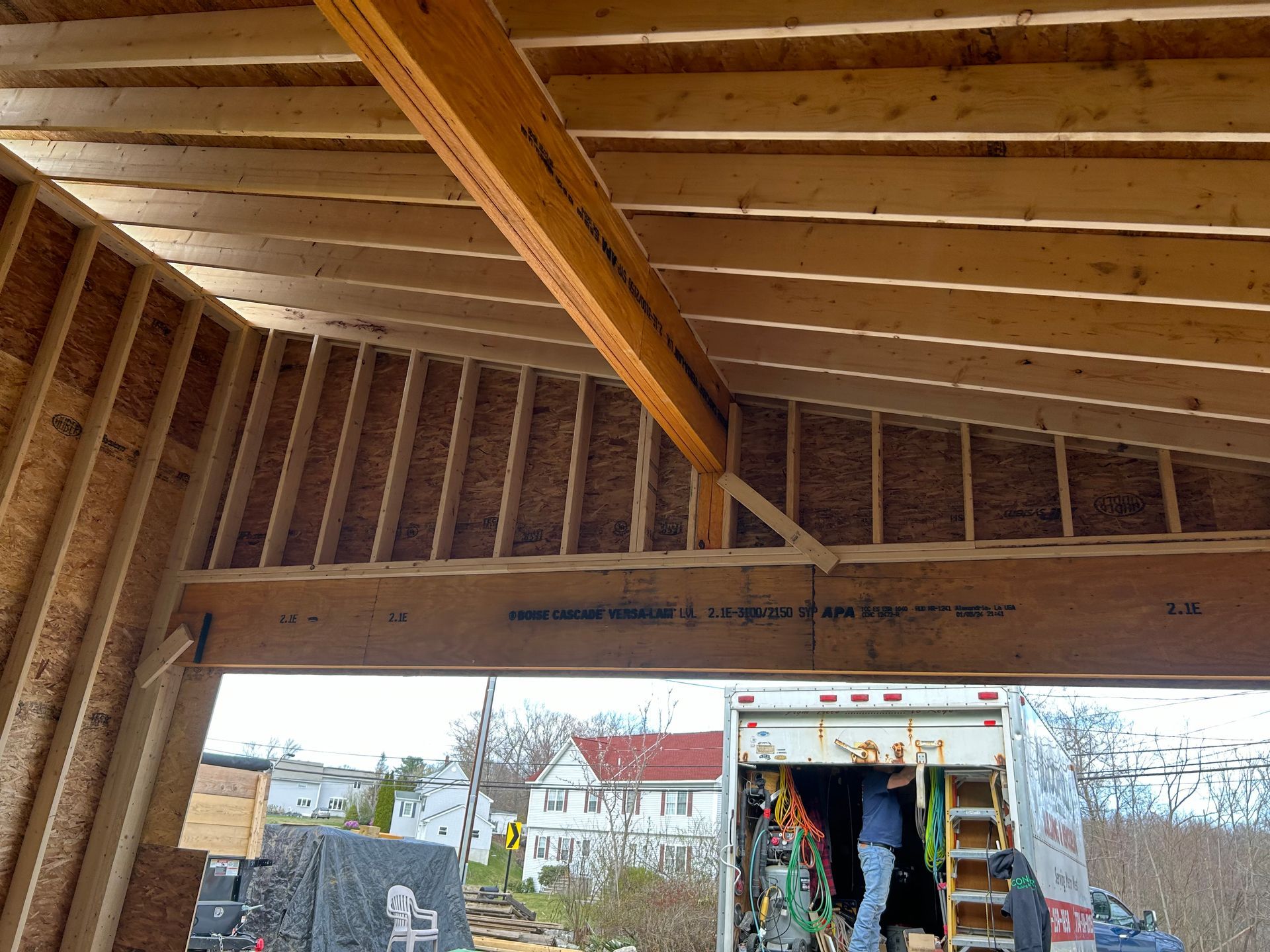 Construction of a wooden building's interior framing. A large beam is overhead. A moving truck is parked outside the building.