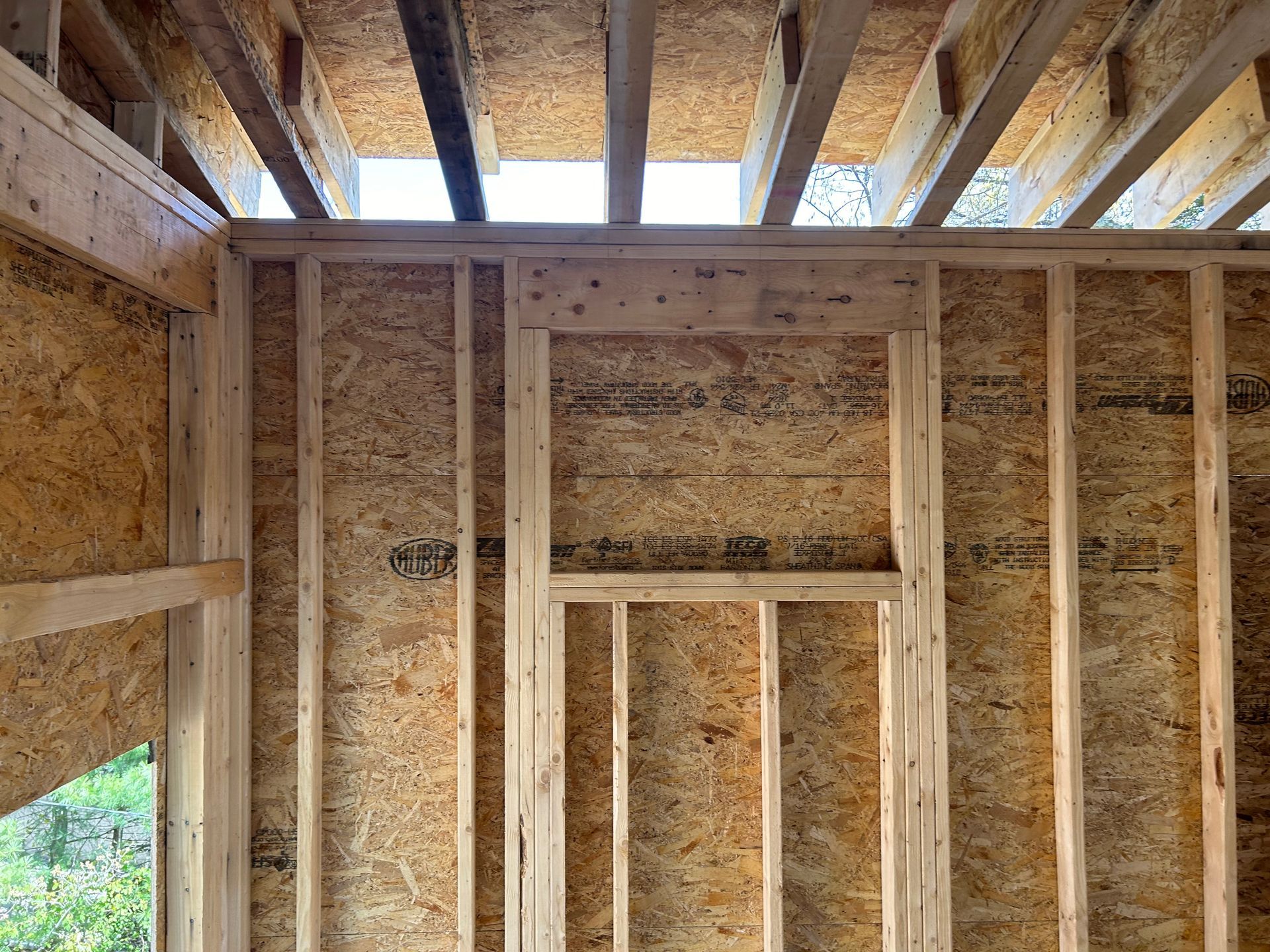 Interior view of a building under construction, showing wooden framing for walls, a window, and exposed ceiling beams.