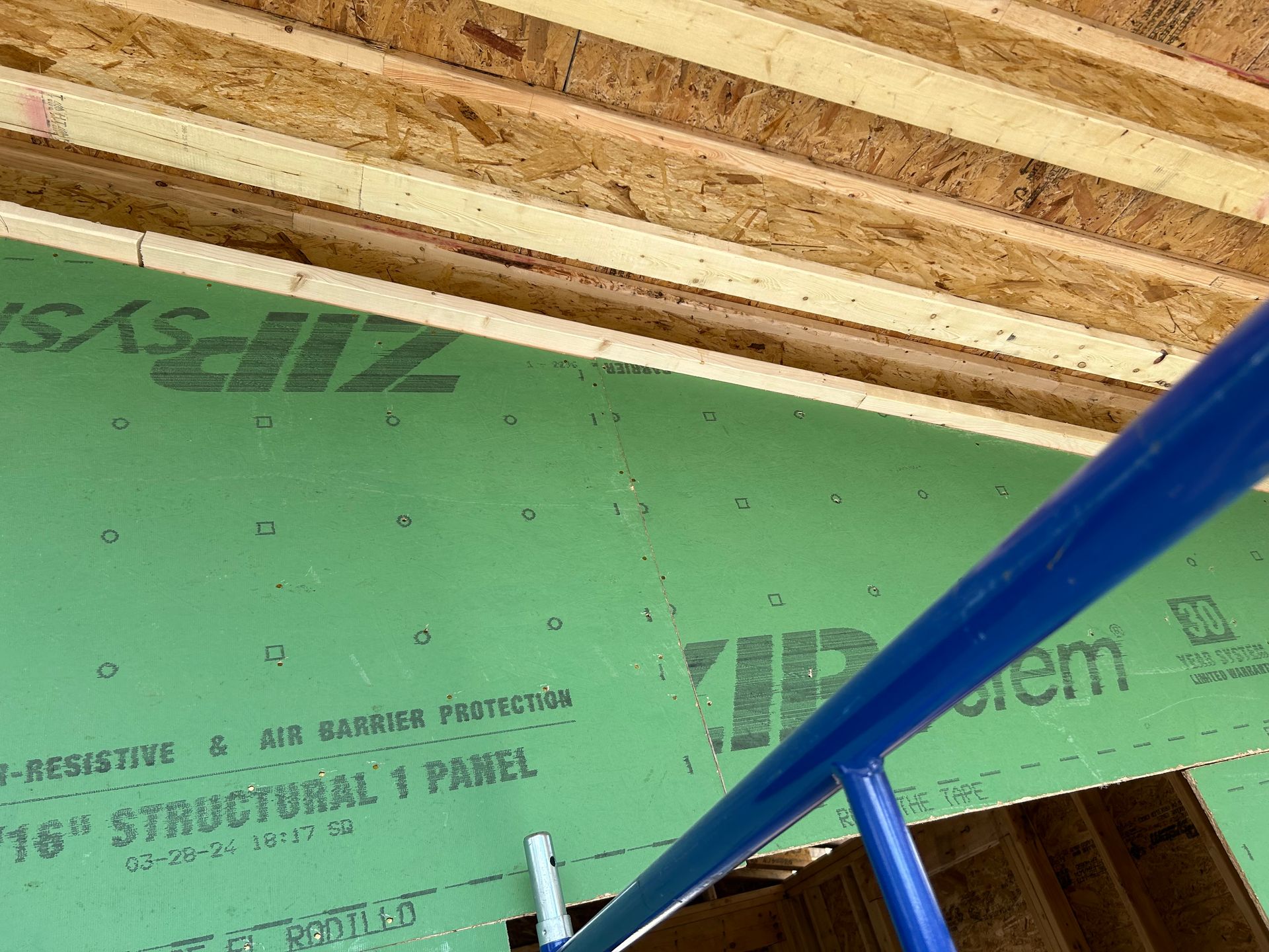Green construction panel with blue scaffolding, attached to wooden ceiling beams.