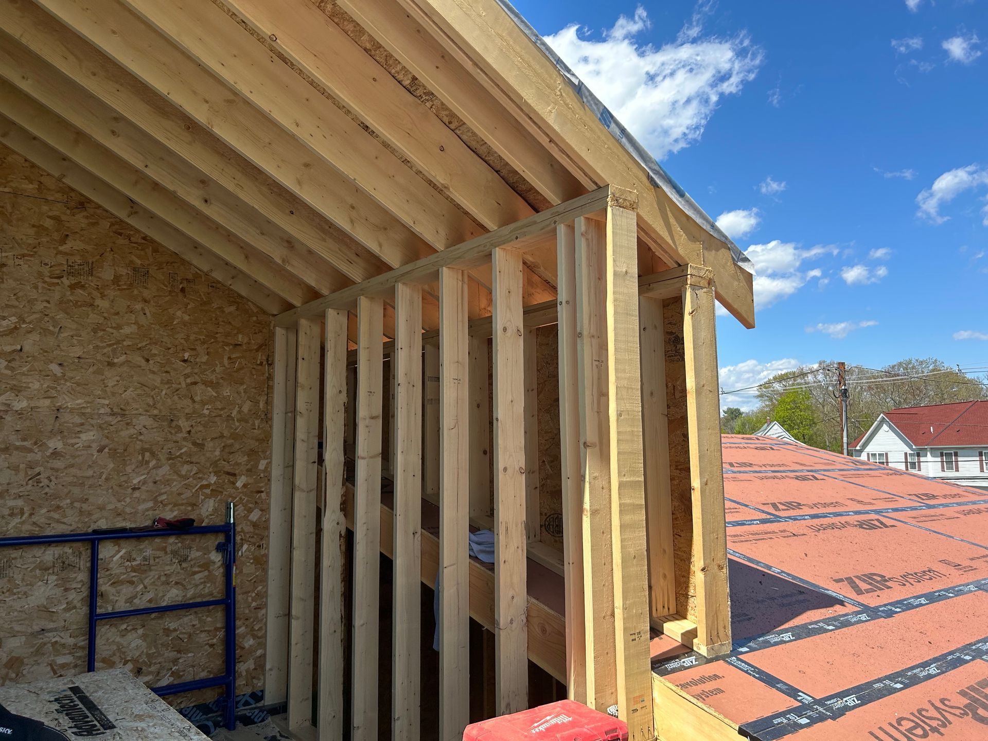 Construction framing for a roof with visible wood beams and vertical studs, under a blue sky.