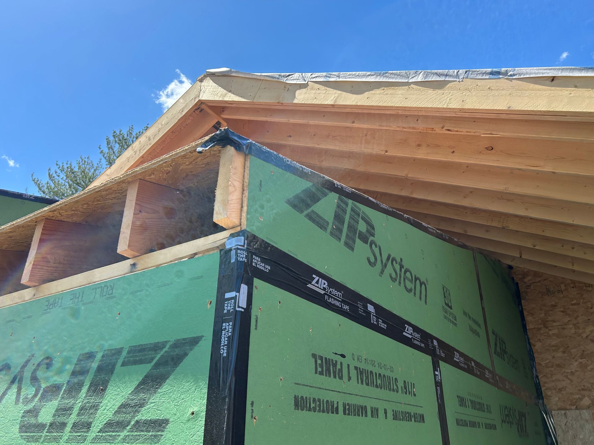 Framing of a house under construction; wood beams and green siding against a blue sky.