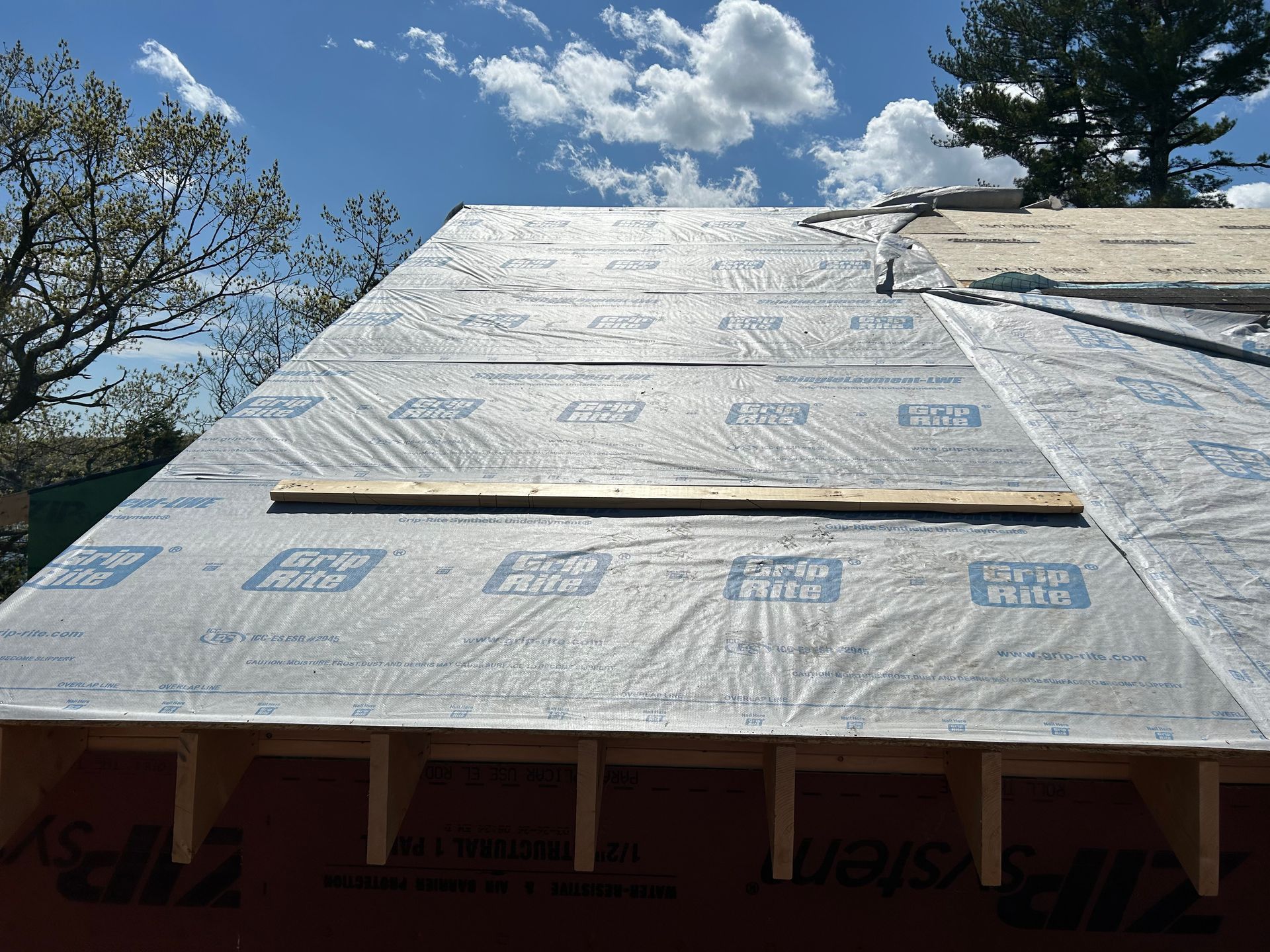 Roof under construction, sheathing covered in protective material, blue sky background.