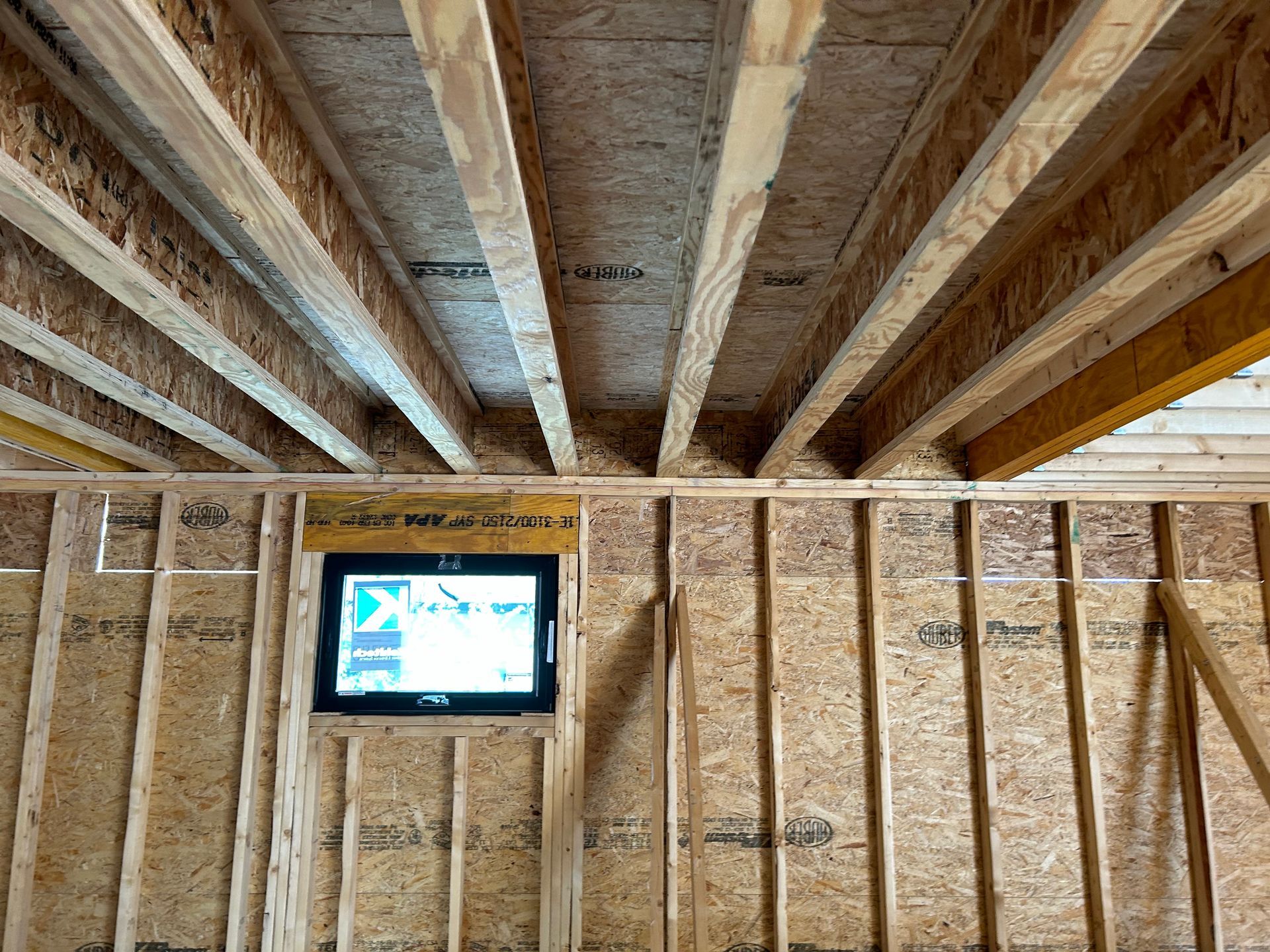 Interior view of a building under construction. Wooden beams and studs are visible, with a small monitor in the wall.