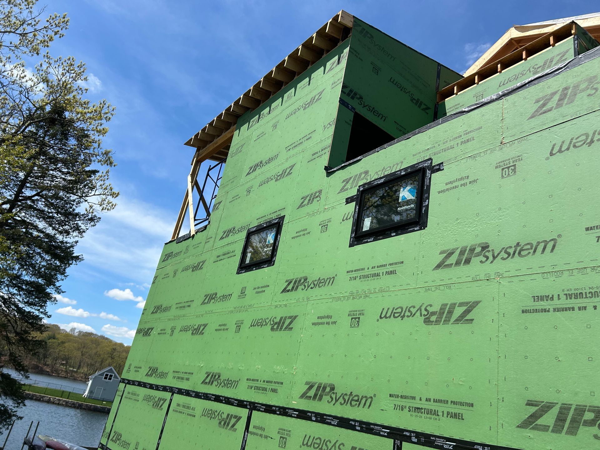 Exterior view of a building under construction, sheathed with green Zip System panels. Windows are installed.