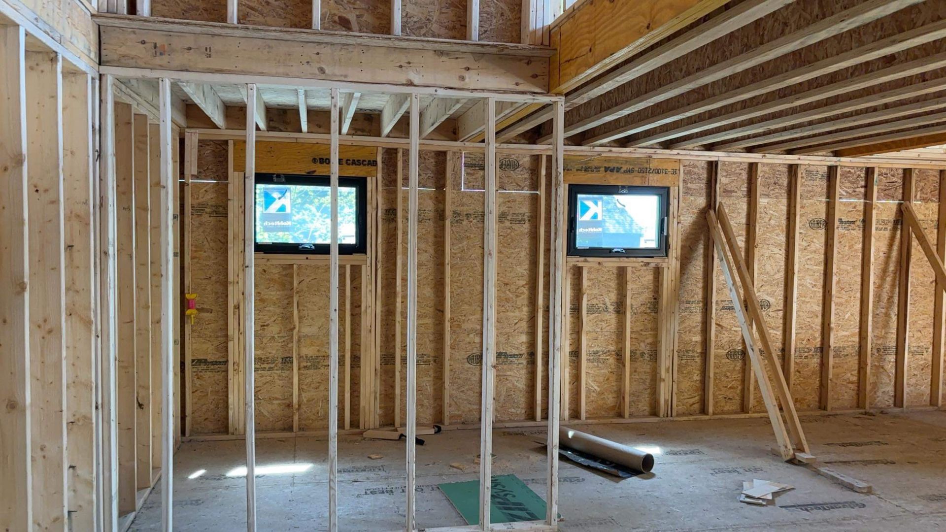 Interior view of a building under construction, showing wooden framing, windows, and ceiling beams.