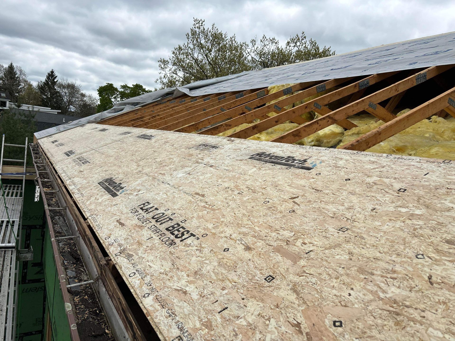 Partially completed roof with exposed rafters, insulation, and new plywood sheathing.