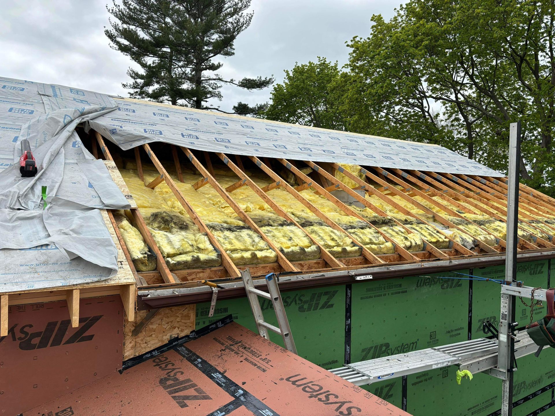 Roof construction: exposed rafters with insulation, covered with waterproof sheeting, and a partially built roof.