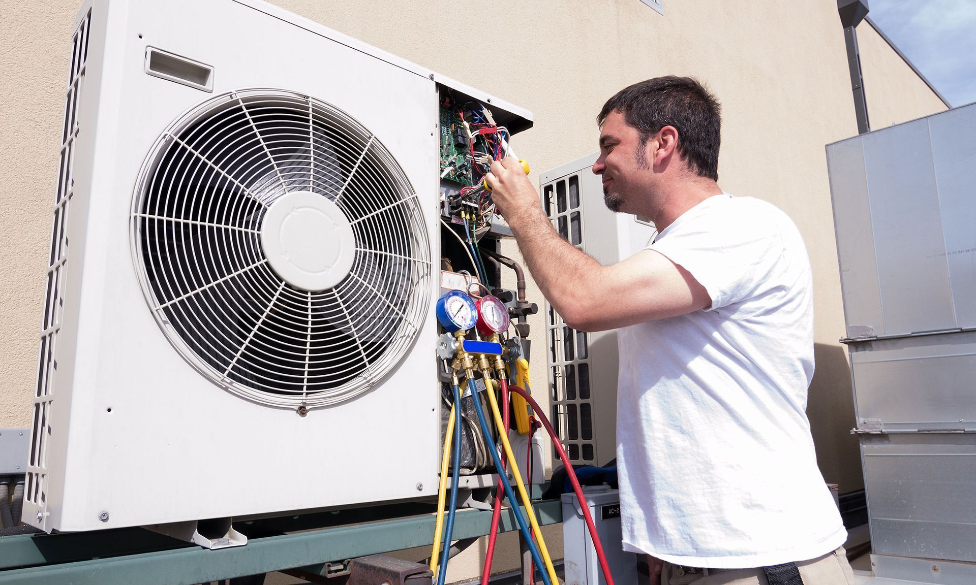 Technician servicing an outdoor air conditioning unit with exposed wiring and tools.