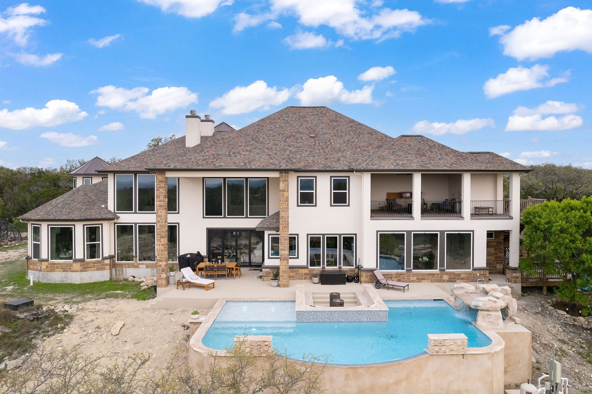 Large two-story house with a pool and stone patio under a blue sky