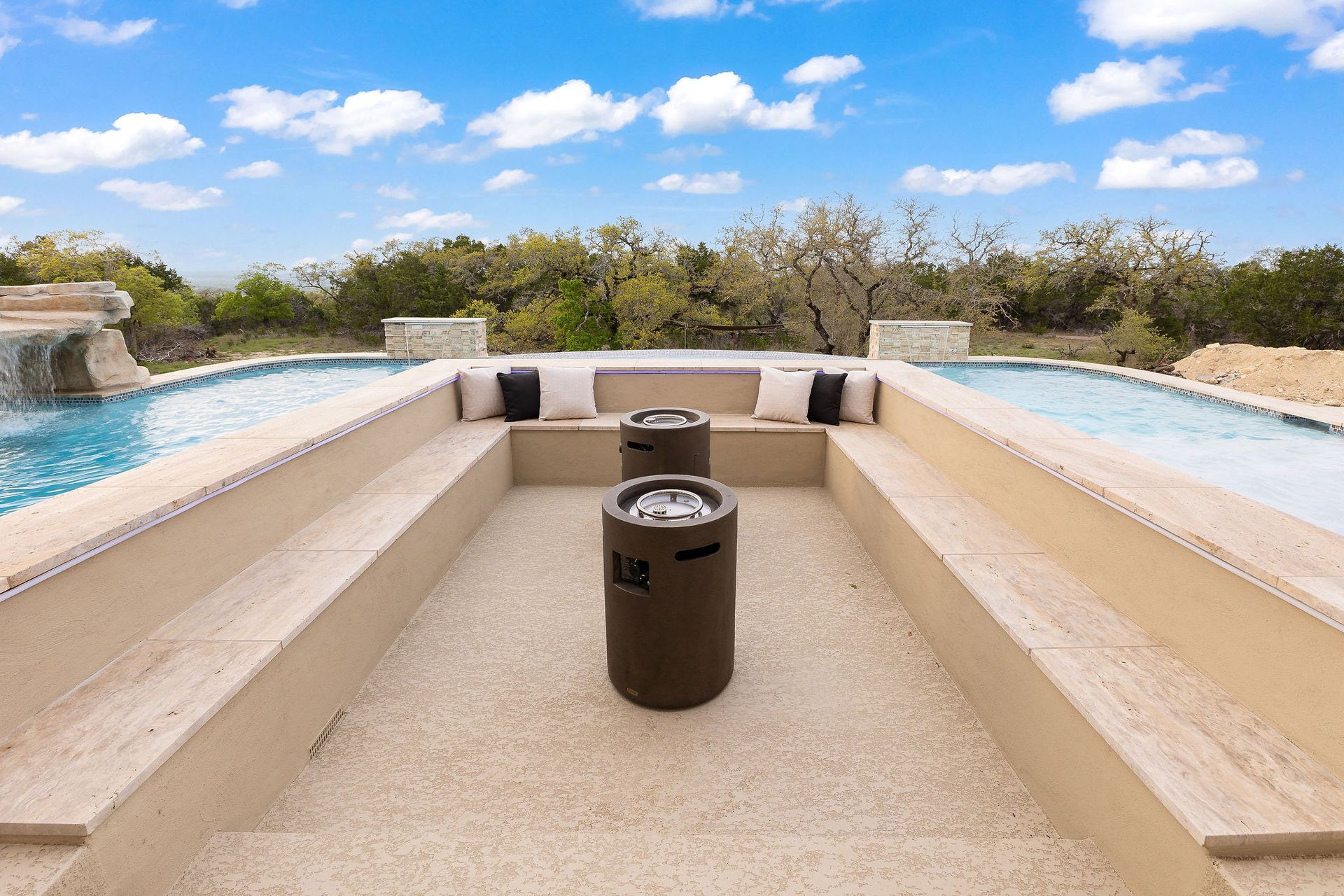 Modern poolside fire pit with beige seating, turquoise water, and blue sky backdrop