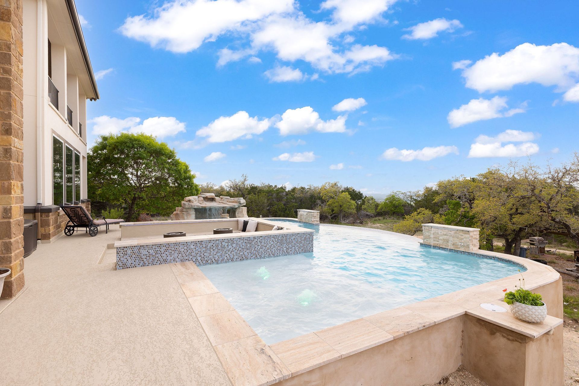 Modern backyard with a turquoise pool, lounge chairs, trees, and a sunset sky over hills.