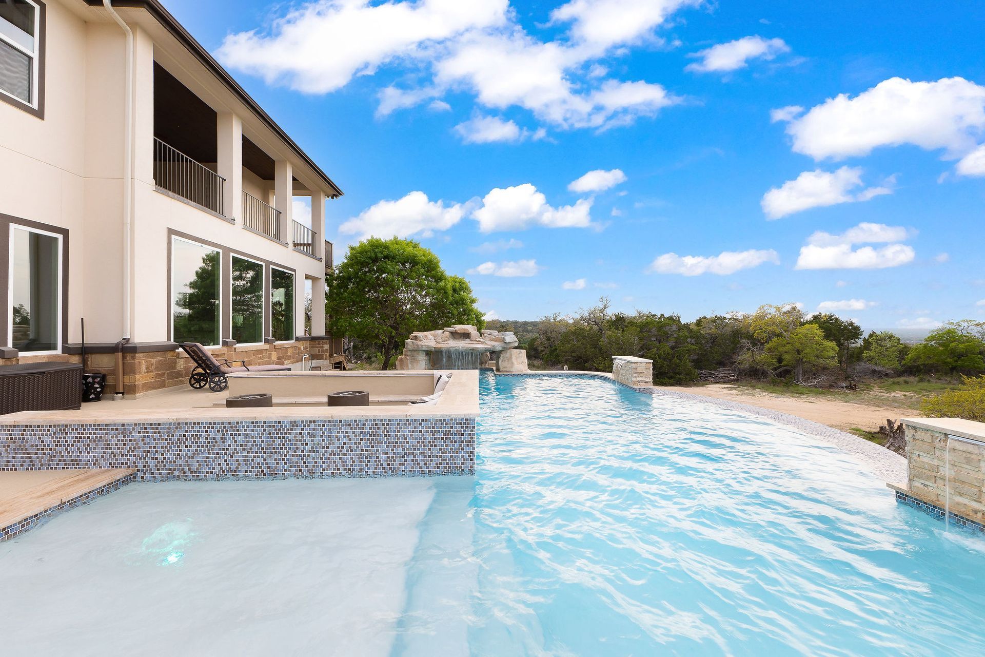 Modern backyard with a turquoise pool, lounge chairs, trees, and a sunset sky over hills.