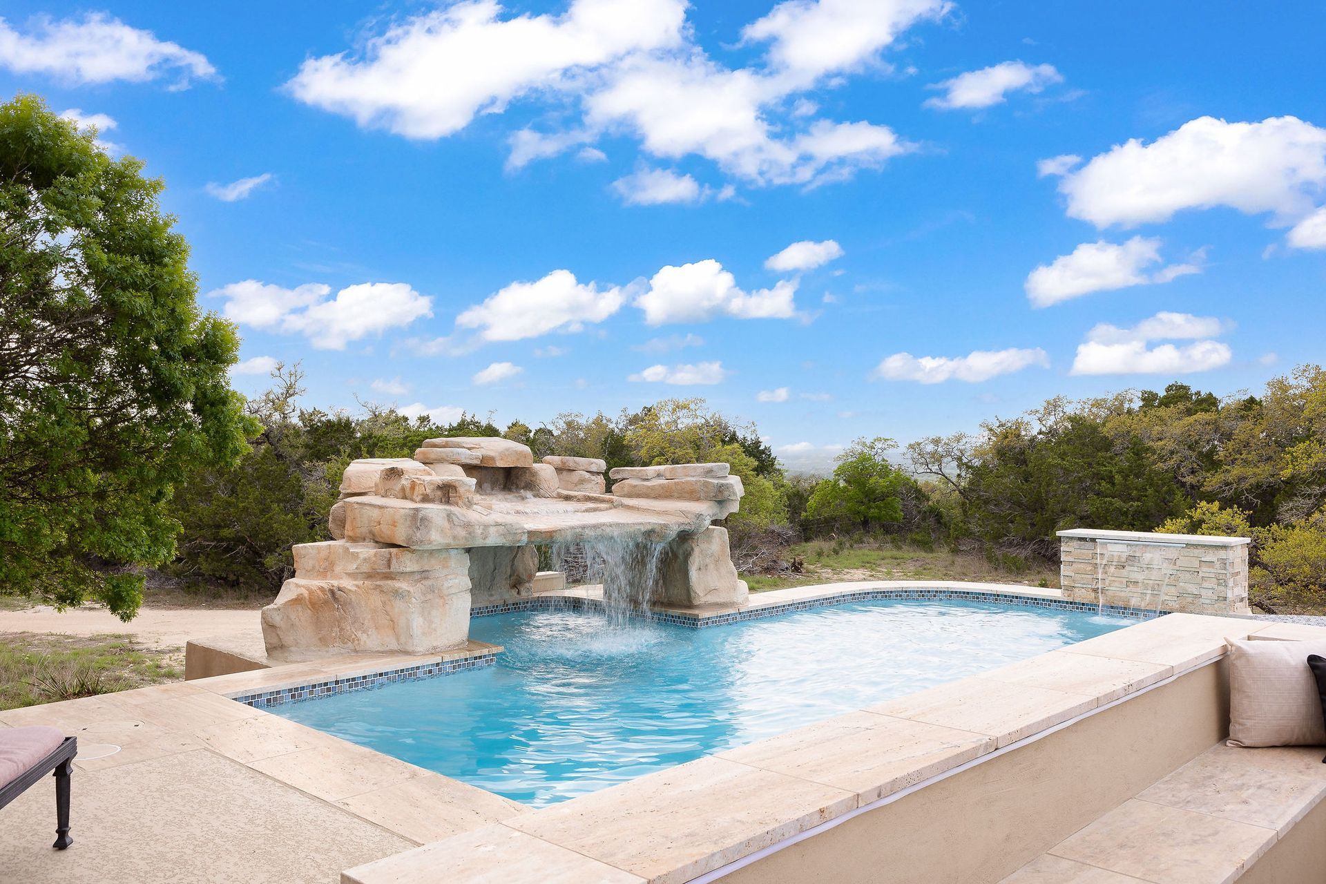 Backyard swimming pool with stone waterfall under a bright blue sky