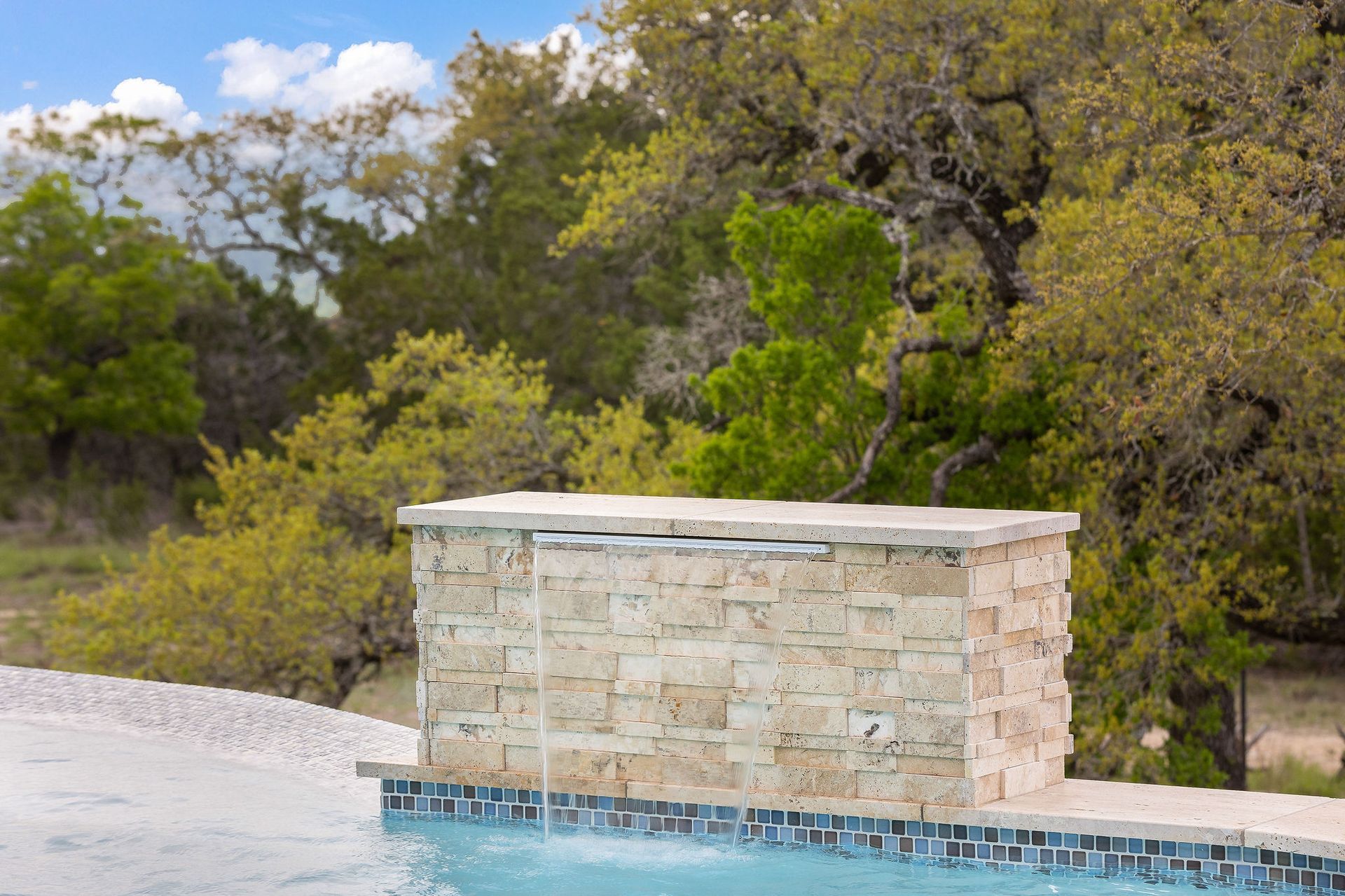 Stone pool fountain beside turquoise water and trees in the background