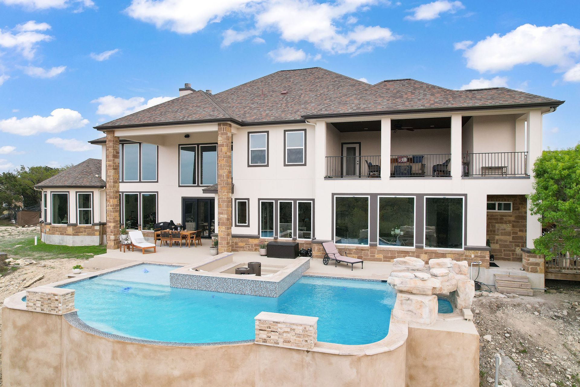 Modern backyard with a turquoise pool, lounge chairs, trees, and a sunset sky over hills.