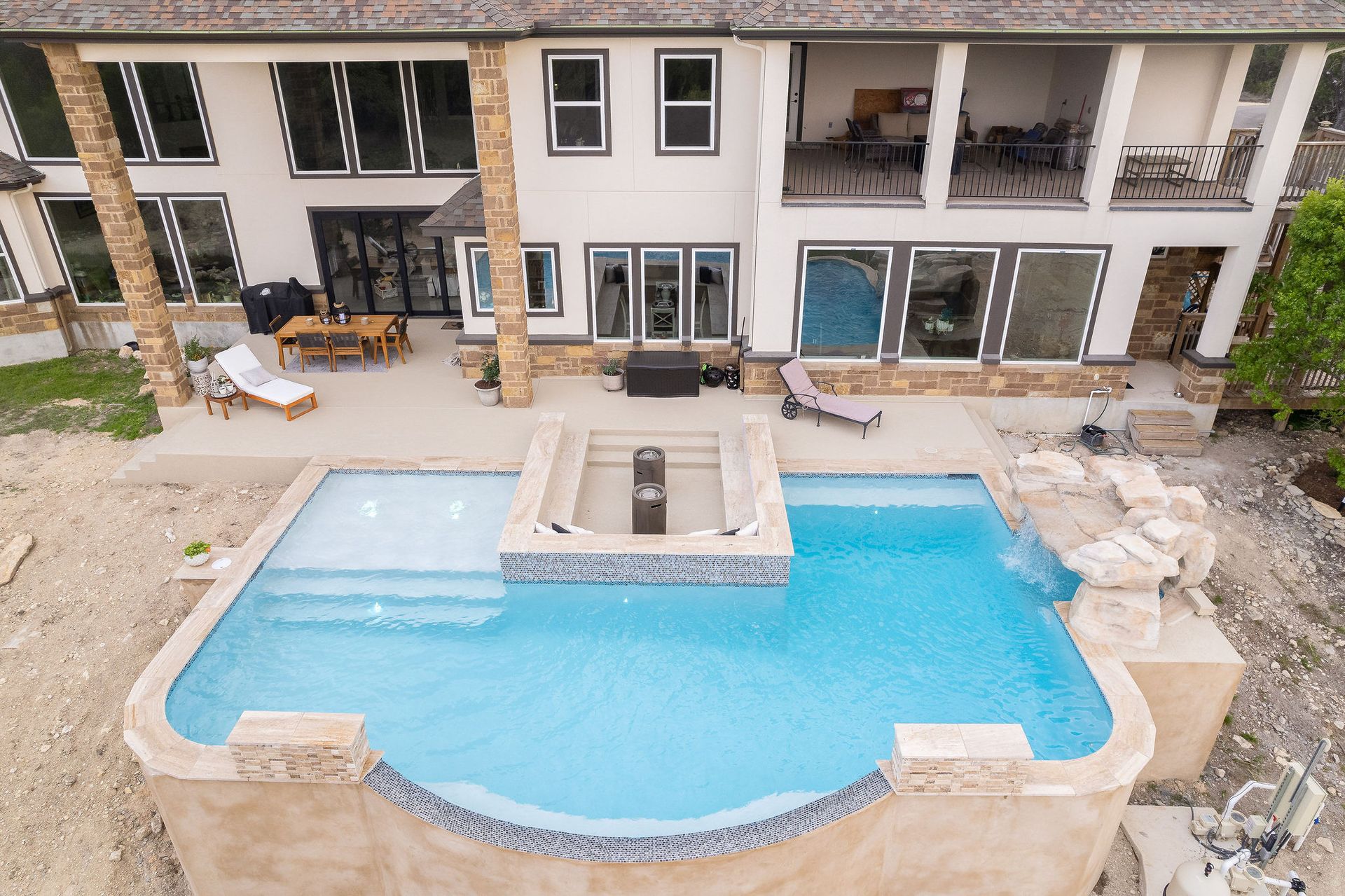Modern backyard with a turquoise pool, lounge chairs, trees, and a sunset sky over hills.
