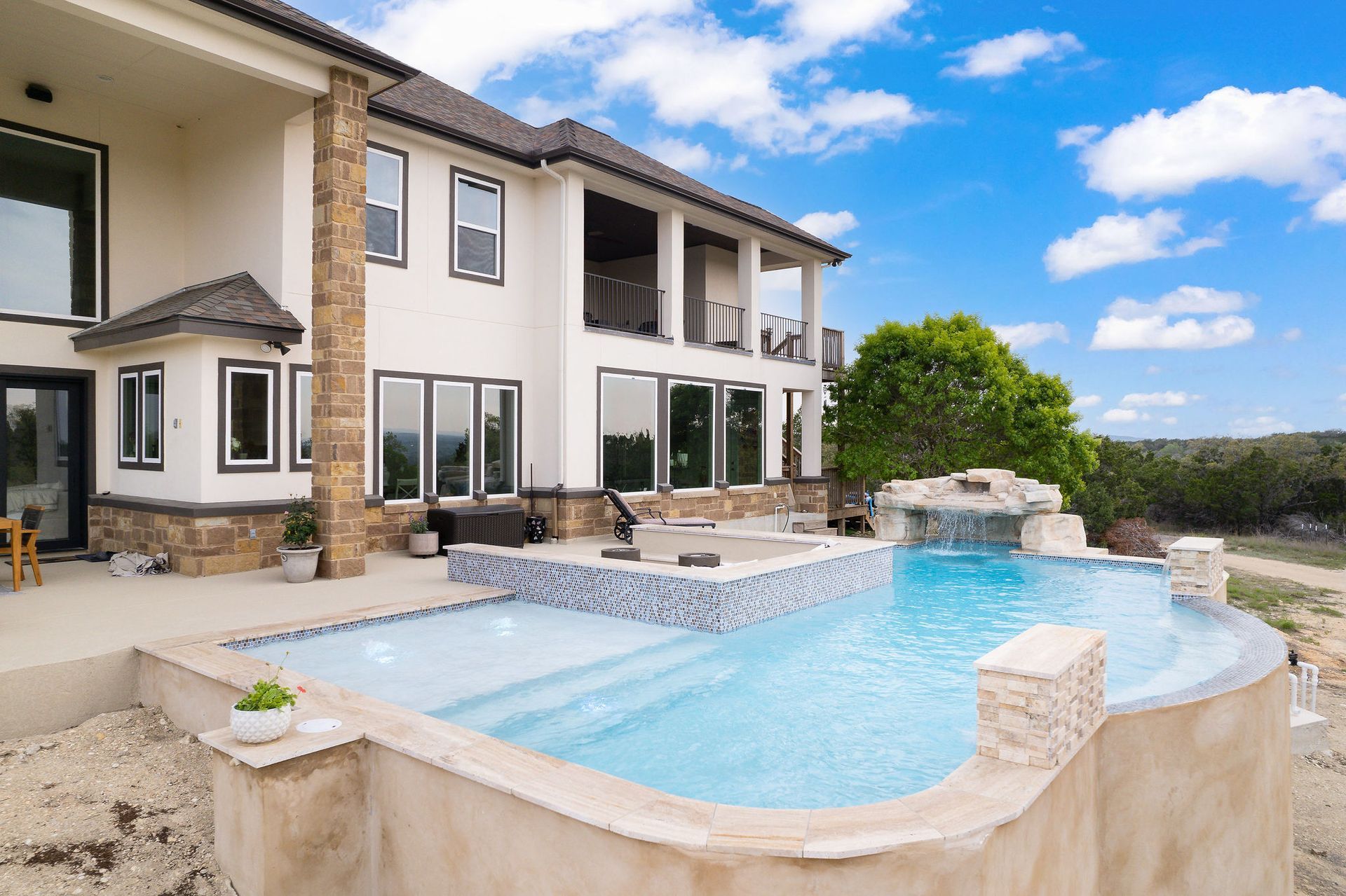 Modern backyard with a turquoise pool, lounge chairs, trees, and a sunset sky over hills.