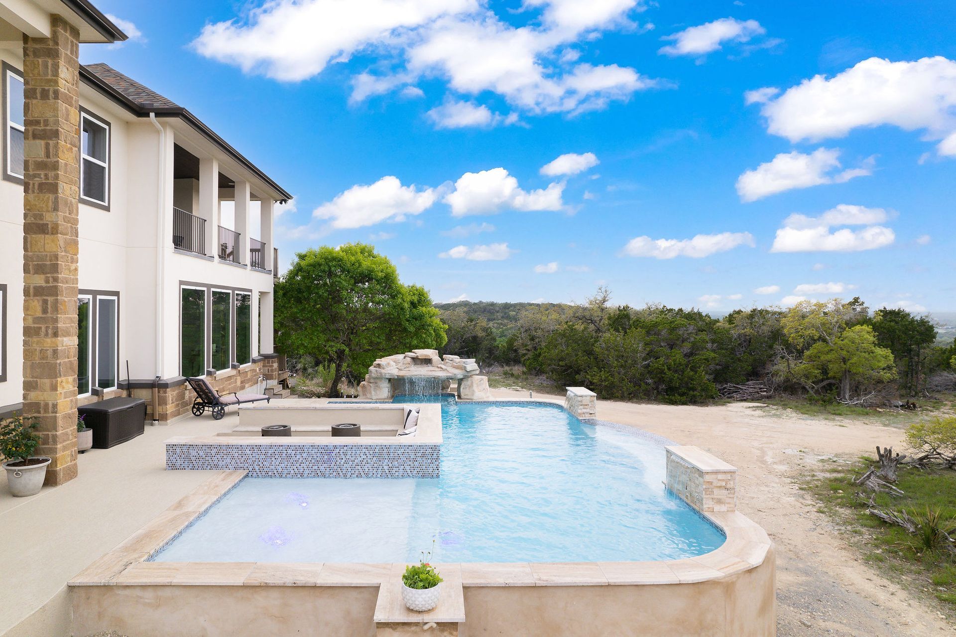Modern backyard with a turquoise pool, lounge chairs, trees, and a sunset sky over hills.