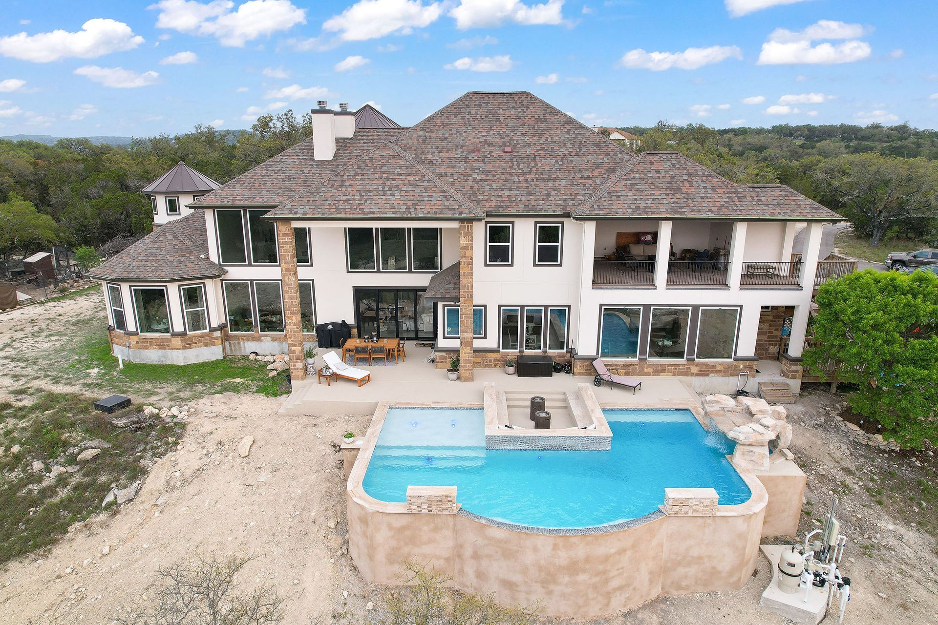 Modern backyard with a turquoise pool, lounge chairs, trees, and a sunset sky over hills.