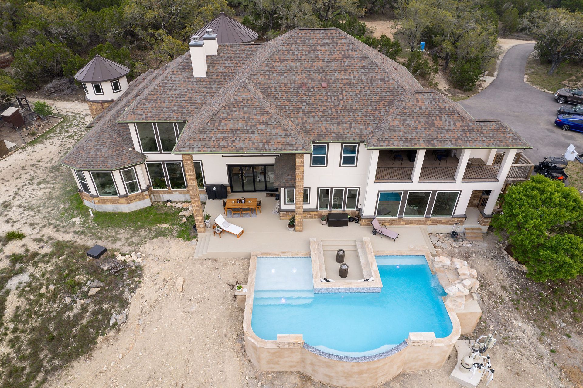 Modern backyard with a turquoise pool, lounge chairs, trees, and a sunset sky over hills.