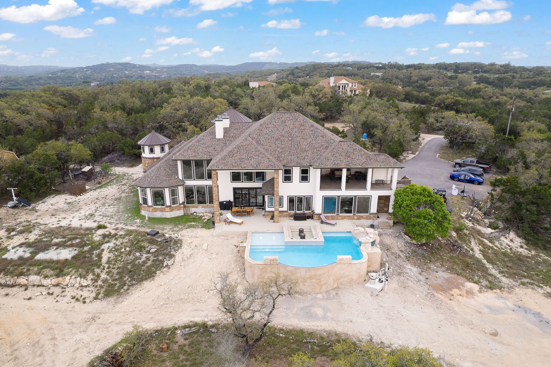Modern backyard with a turquoise pool, lounge chairs, trees, and a sunset sky over hills.