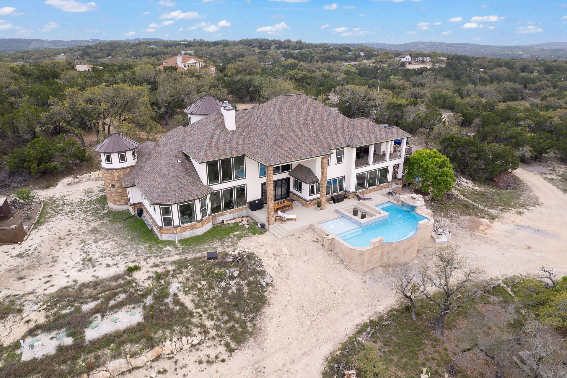 Modern backyard with a turquoise pool, lounge chairs, trees, and a sunset sky over hills.