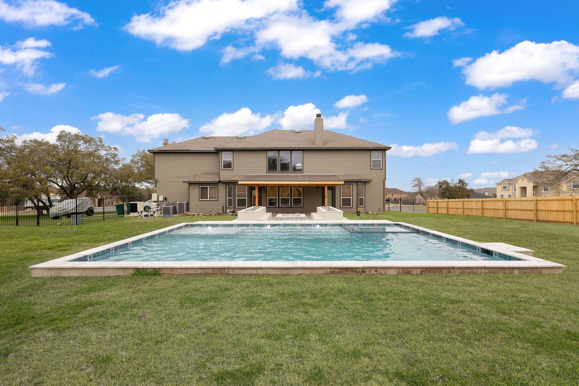 Backyard pool in front of a beige two-story house under a blue sky