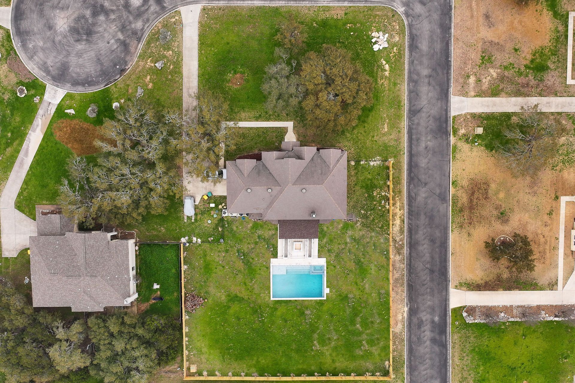 Aerial view of two houses with green lawns, a driveway, and a backyard pool.