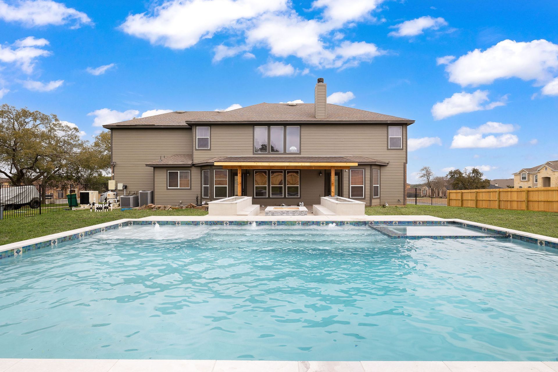 Backyard pool facing a two-story house under a blue sky