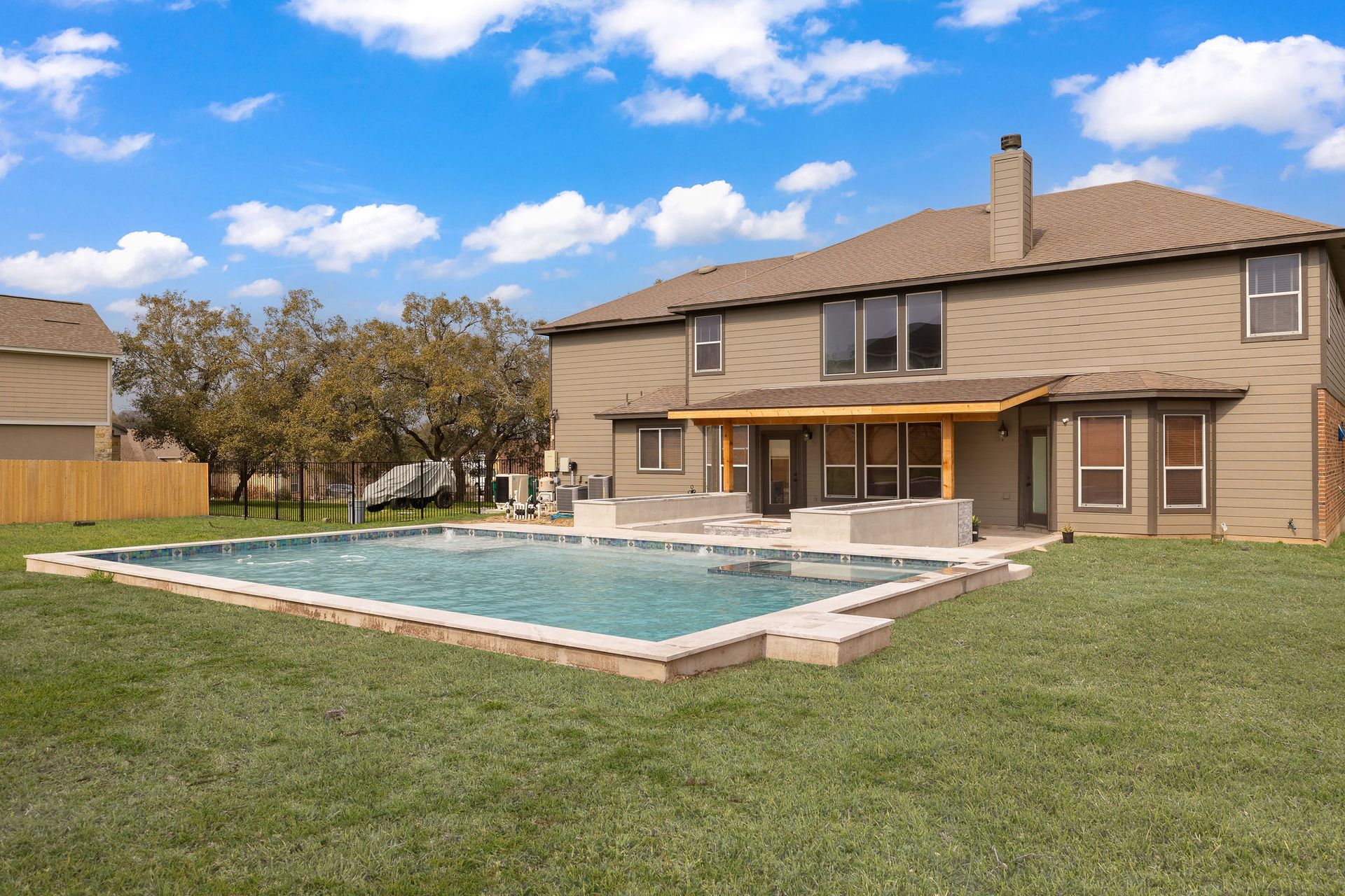 Modern backyard with a turquoise pool, lounge chairs, trees, and a sunset sky over hills.