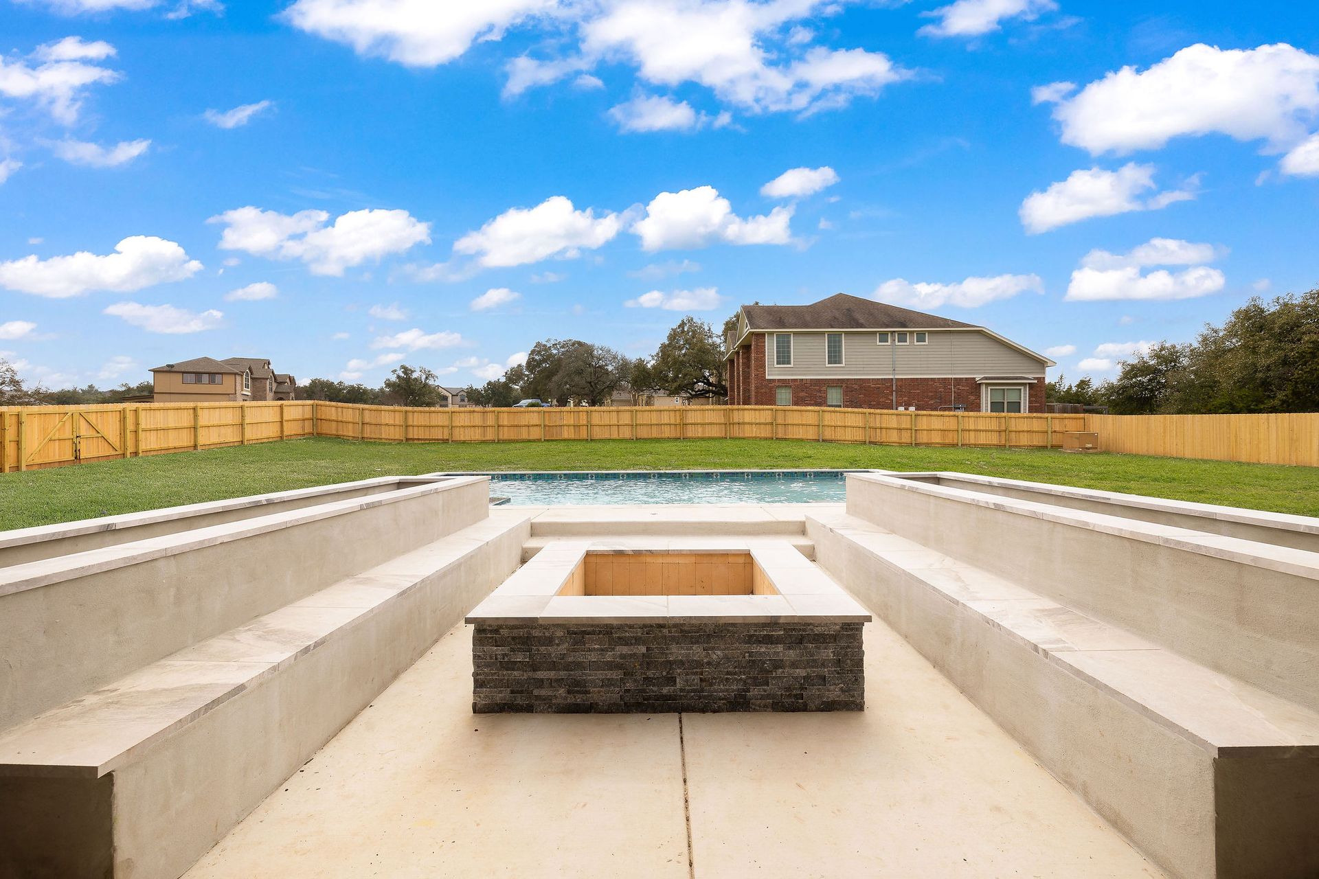 Modern backyard patio with built-in concrete benches and a central fire pit under a blue sky