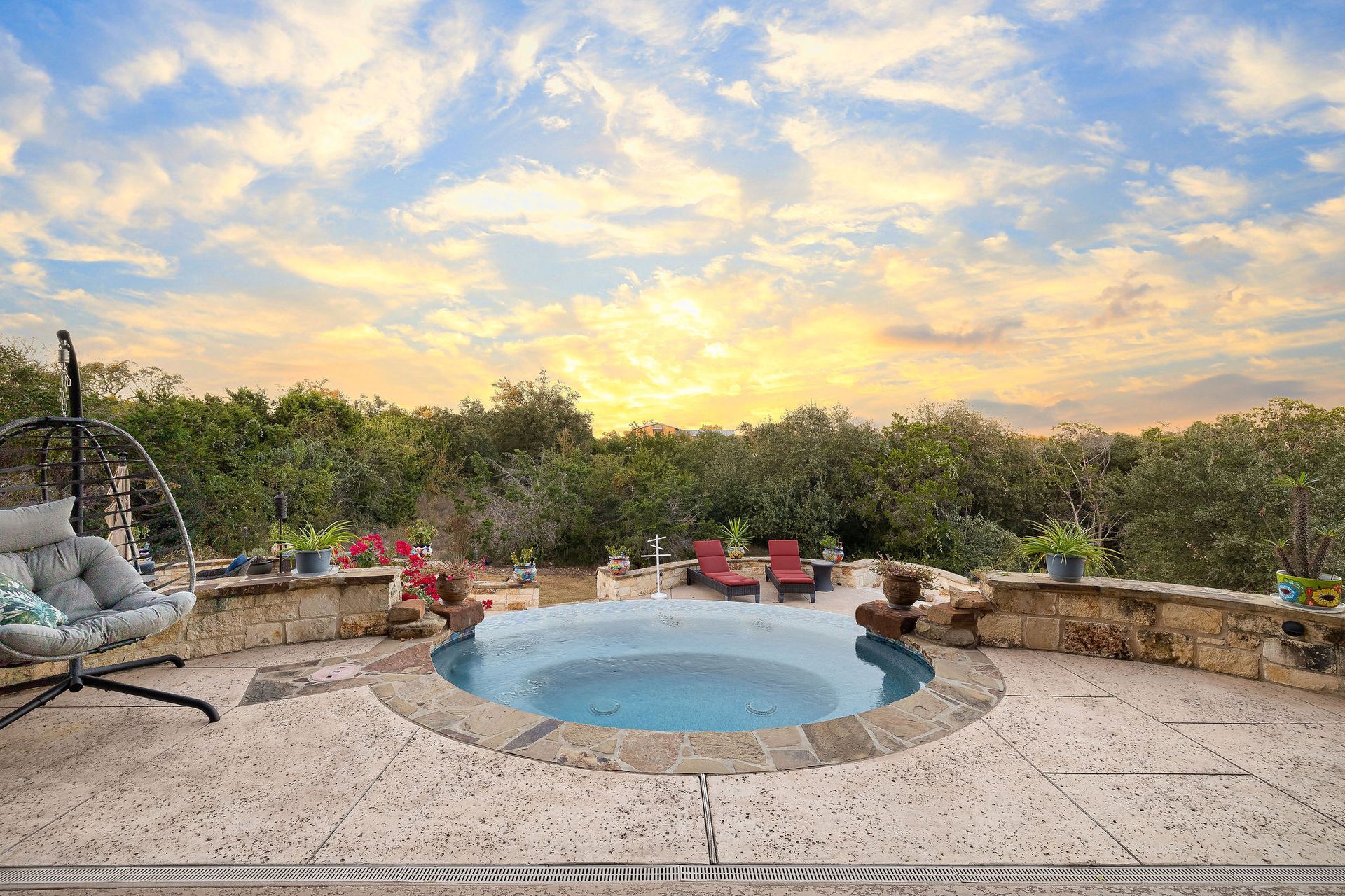 Patio with a small round pool at sunset, surrounded by chairs, plants, and a stone wall.