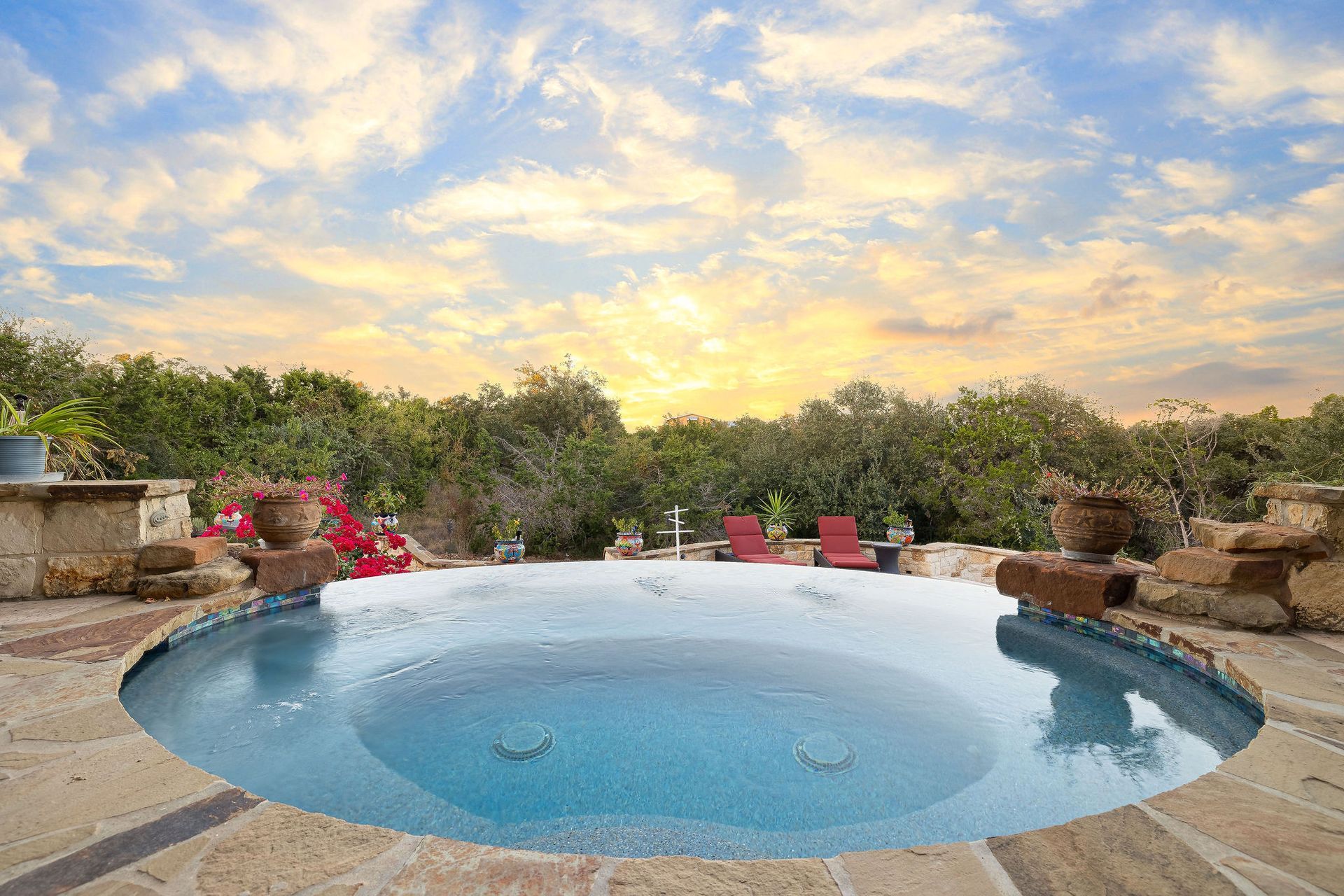Backyard pool at sunset with chairs, potted plants, and a cloudy sky