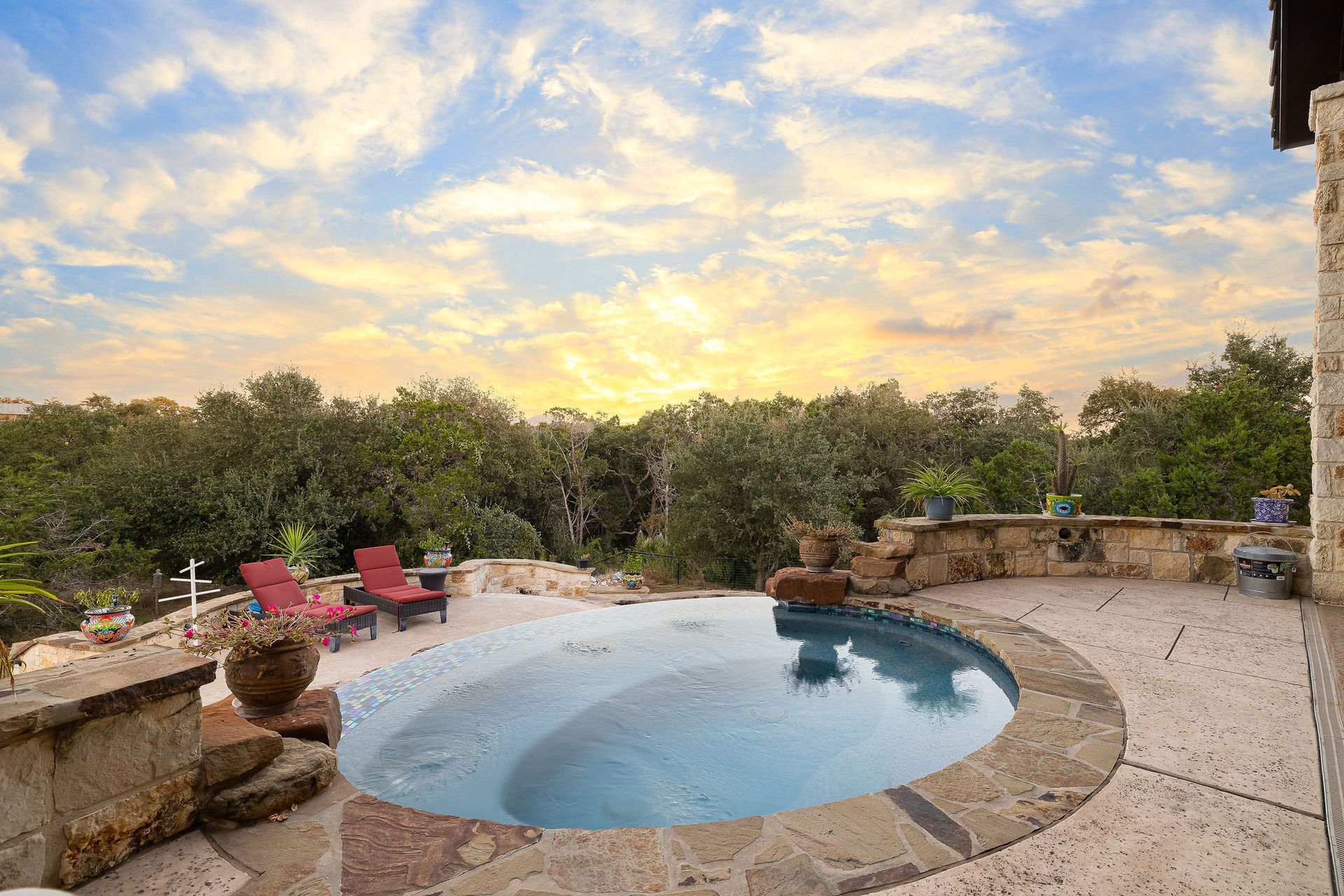 Backyard pool at sunset with chairs, potted plants, and a cloudy sky