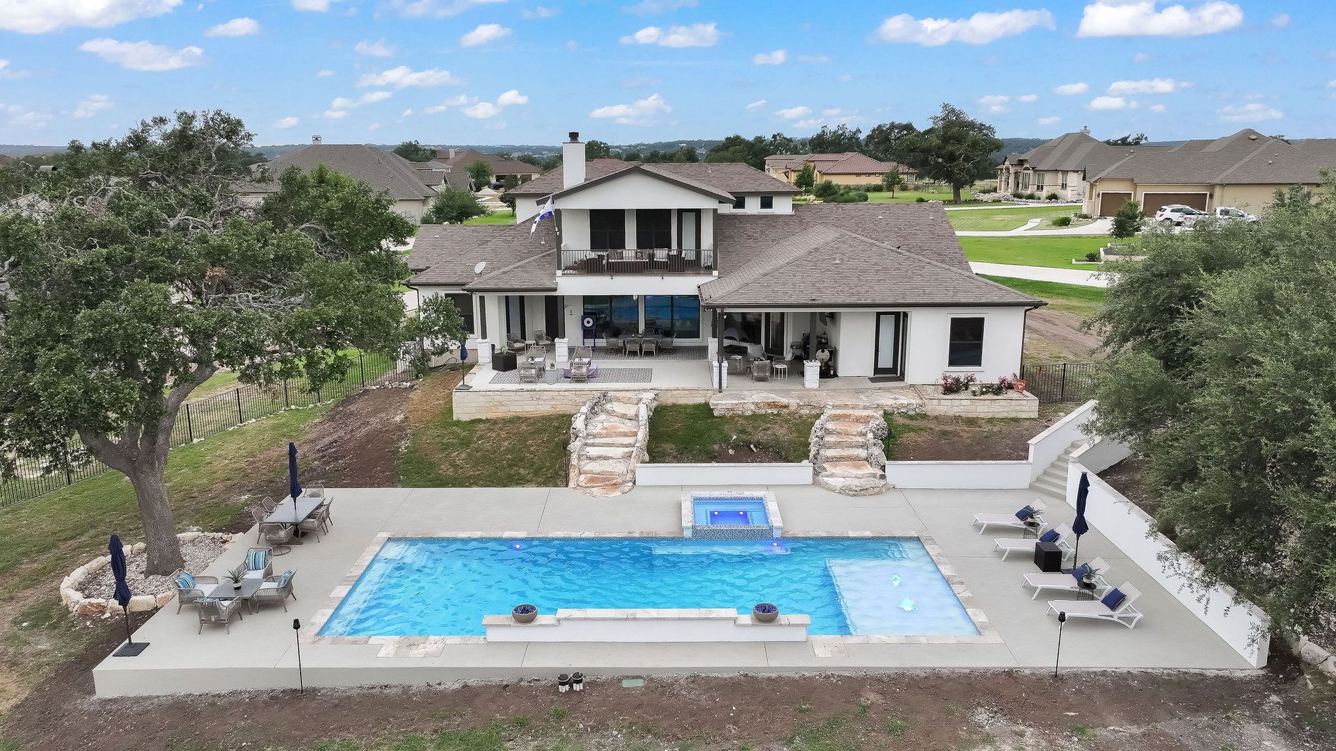 Aerial view of a suburban home with a backyard pool, patio seating, and landscaped yard.