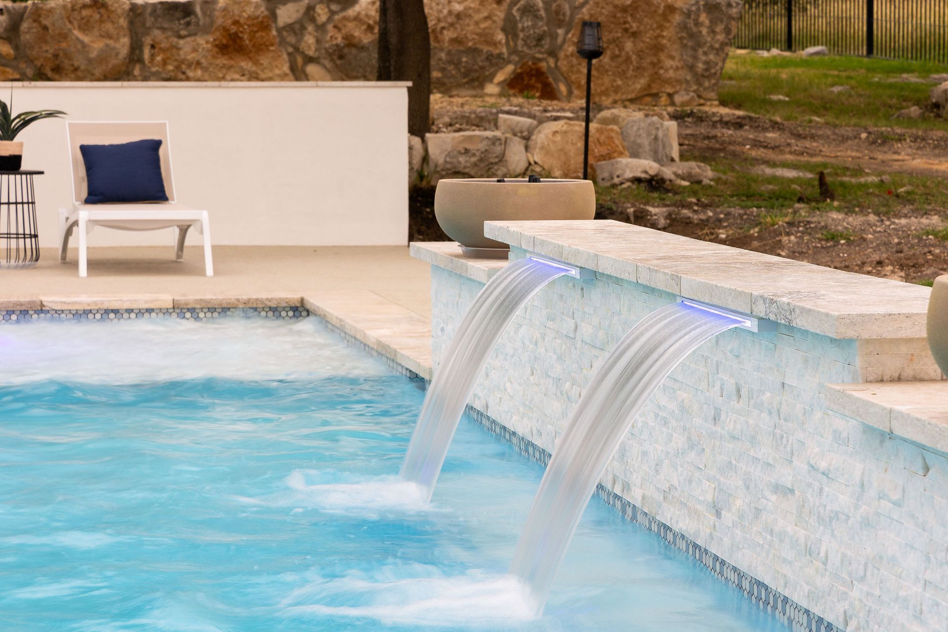 Luxury pool with blue water, tiled edge, and a small waterfall spilling over a stone wall