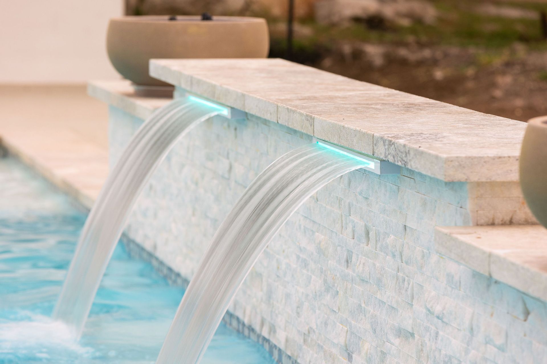 Modern pool fountain with two streams of water spilling over a light stone edge