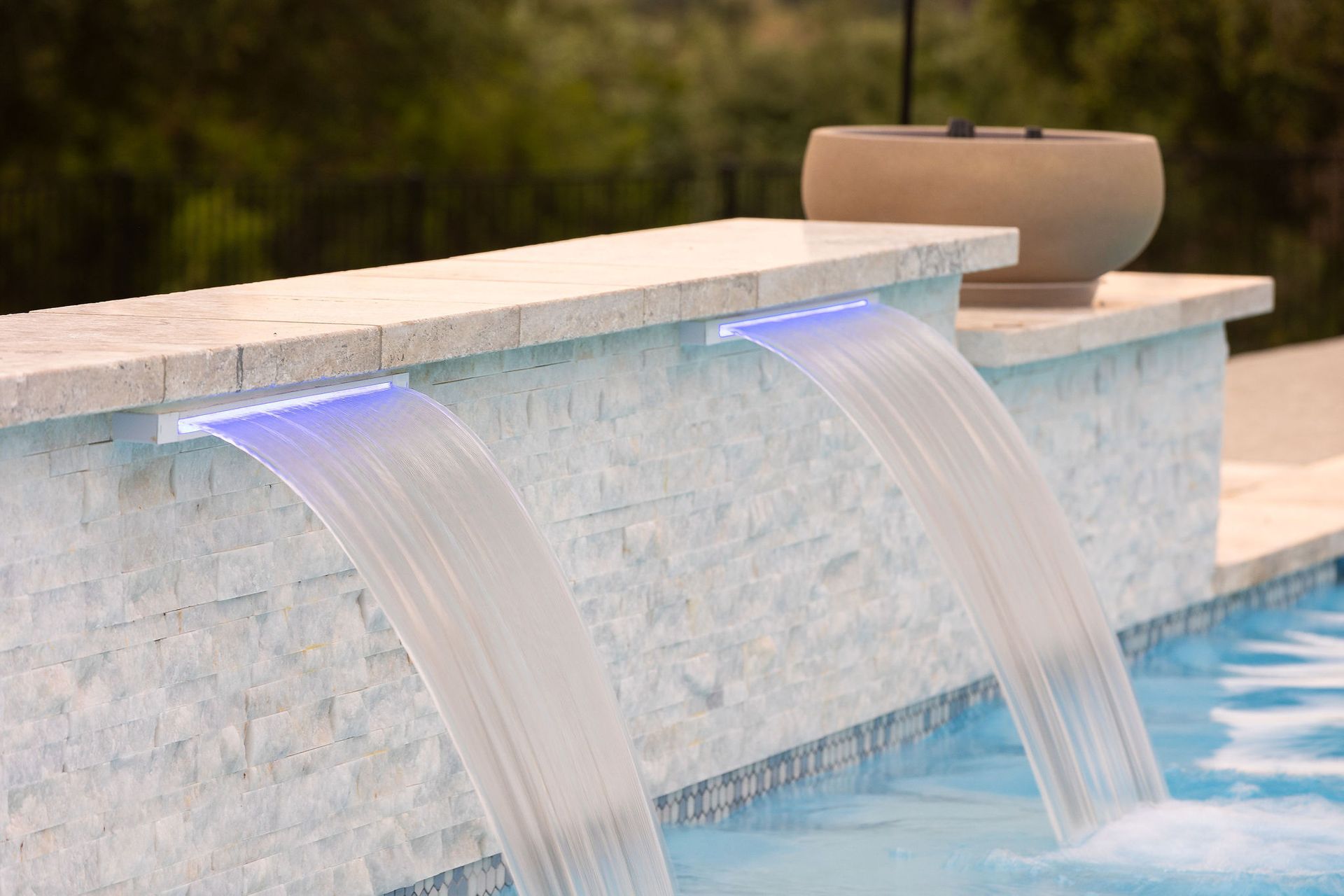 Two water streams spill from a stone fountain into a pool, with a blurred green background