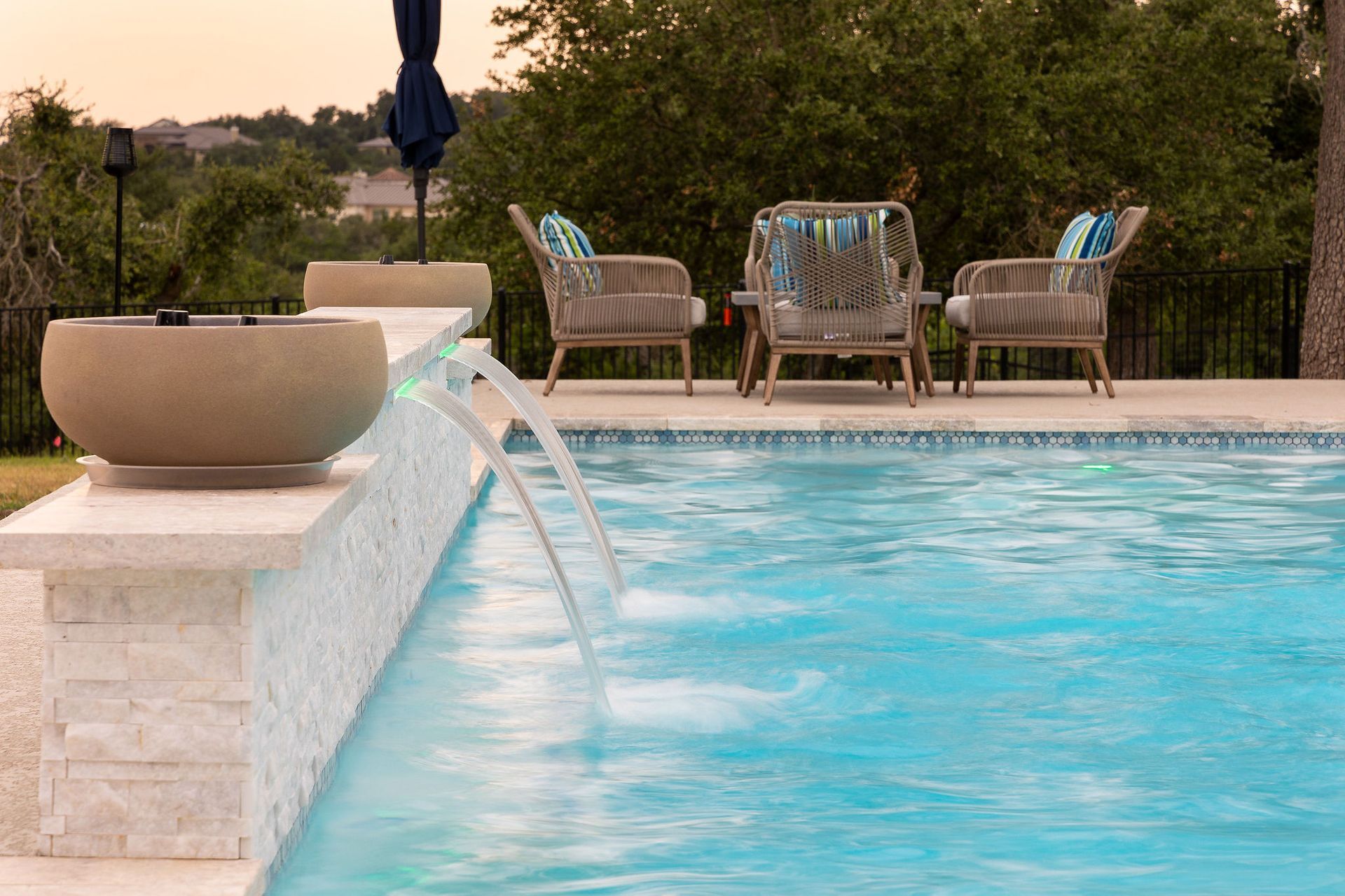 Backyard pool with stone water feature, blue water, and patio chairs in the background