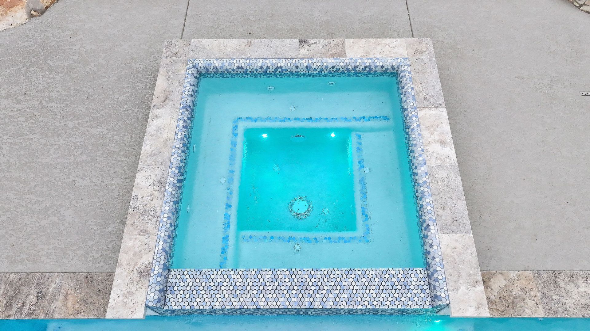 Pool with flowing water spouts beside a white lounge chair and stone patio
