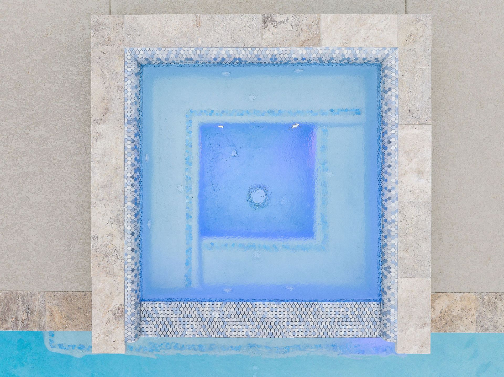 Blue-lit square fountain set into a stone wall with a tiled basin below