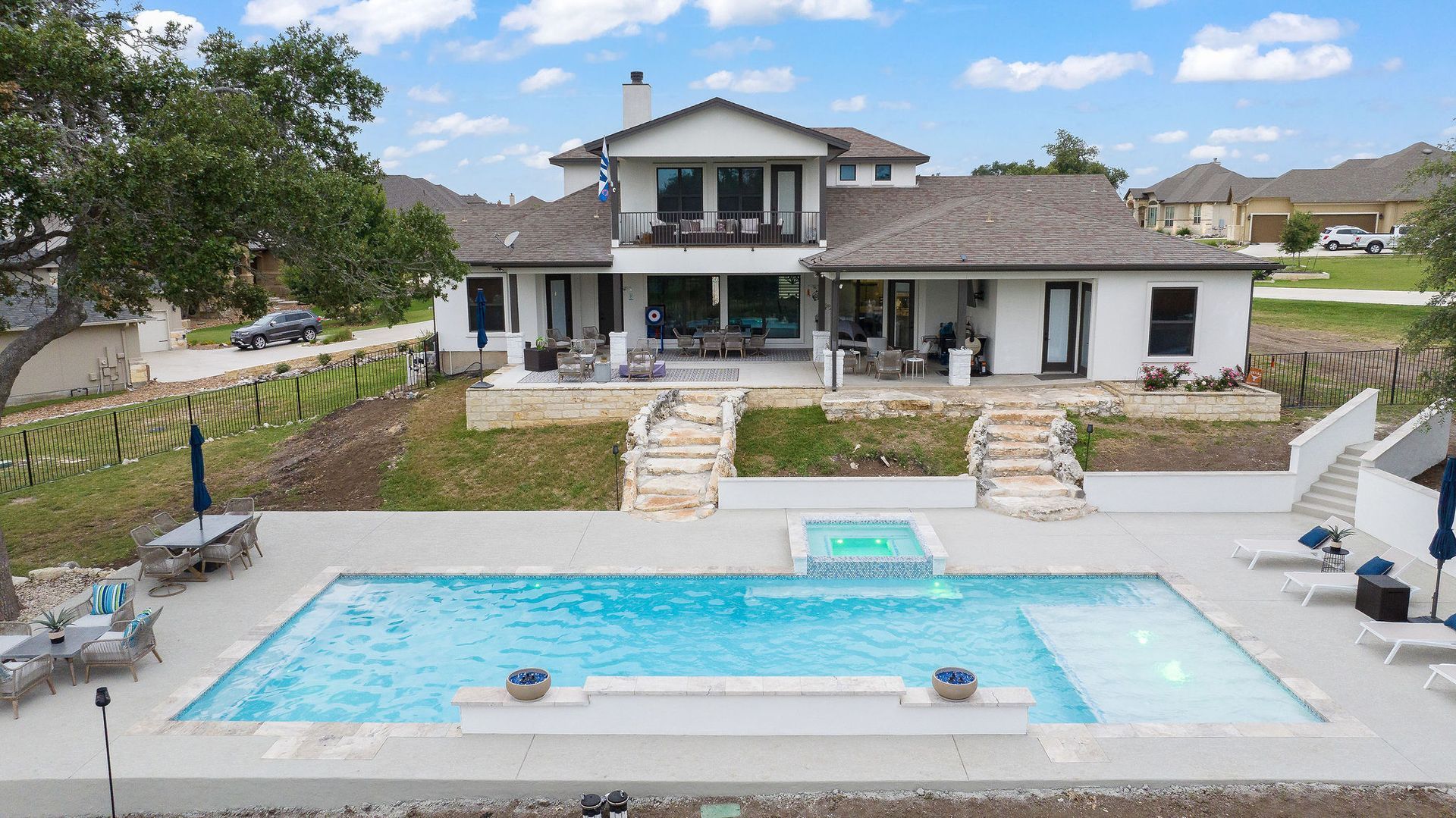 Modern house with a backyard pool, stone patio, and landscaped lawn under a blue sky