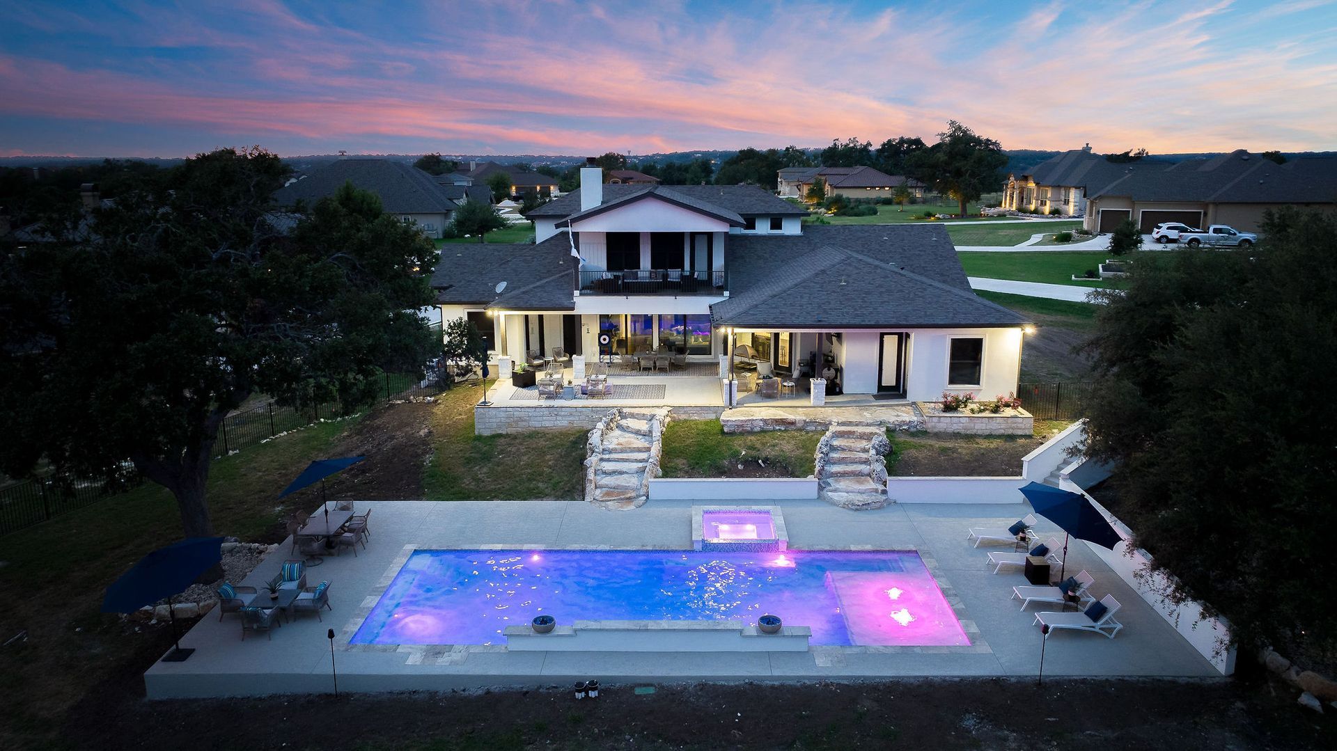 Modern house at dusk with a lit backyard pool and patio under a pink-blue sky