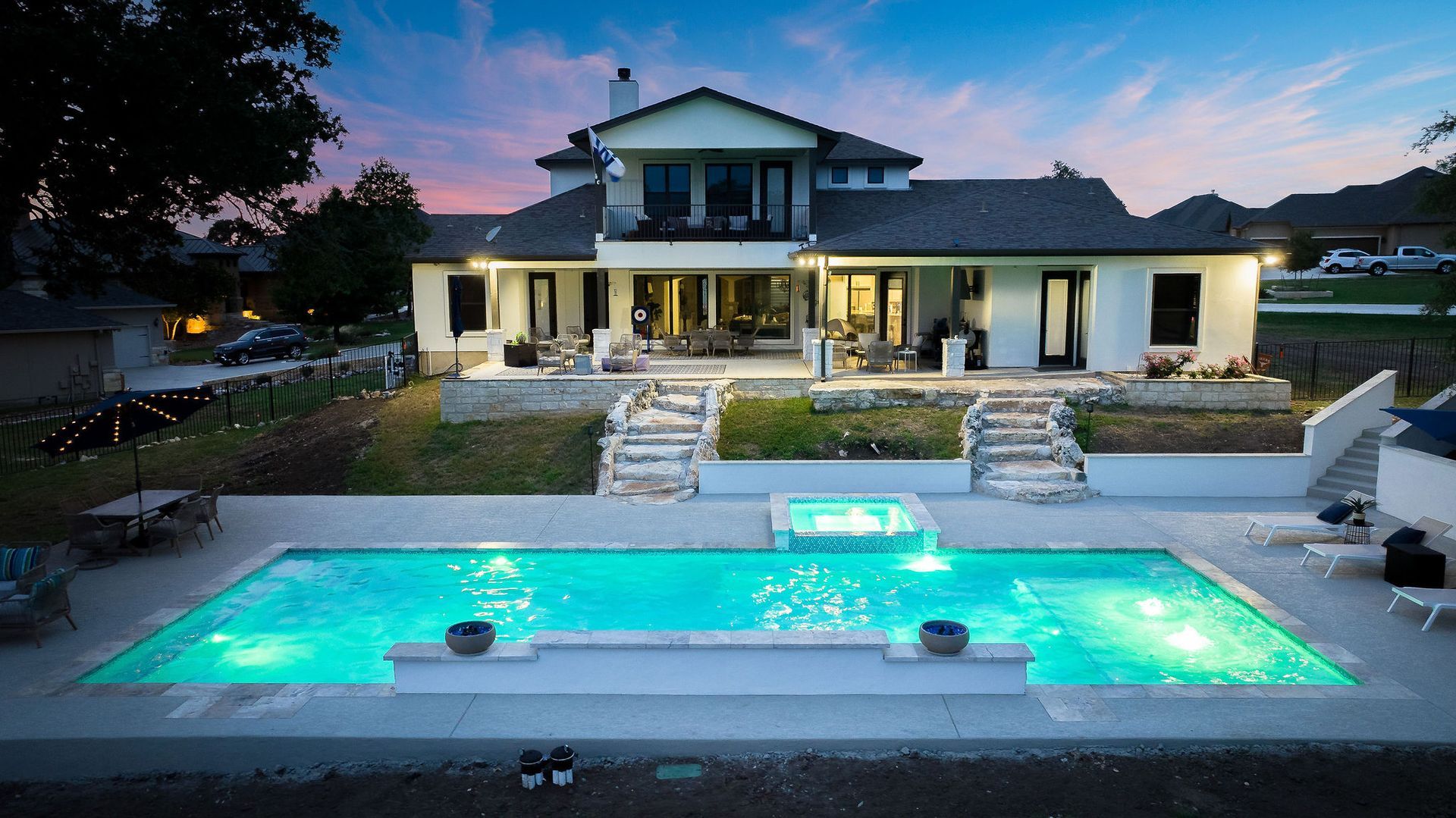 Luxurious backyard pool with glowing turquoise water in front of a modern house at dusk
