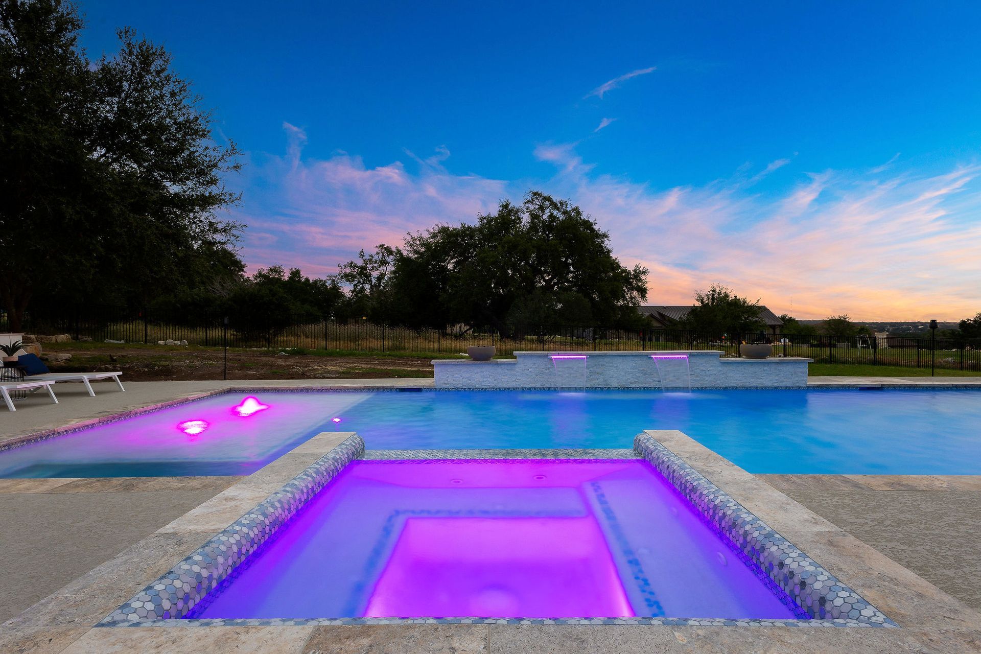 Modern pool with glowing purple lights at dusk, reflecting a blue and pink sunset sky.