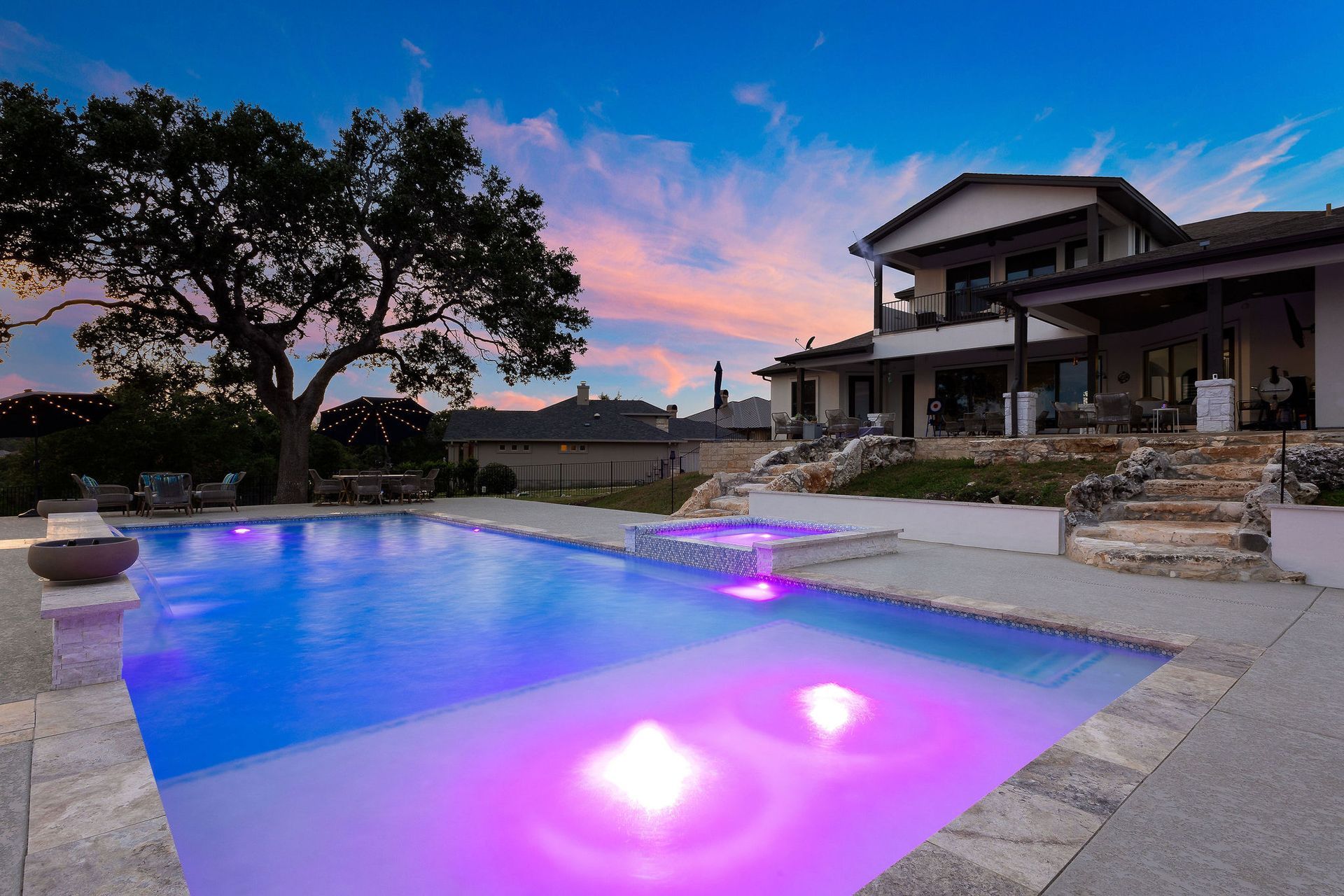 Modern home beside a glowing blue-purple backyard pool at dusk