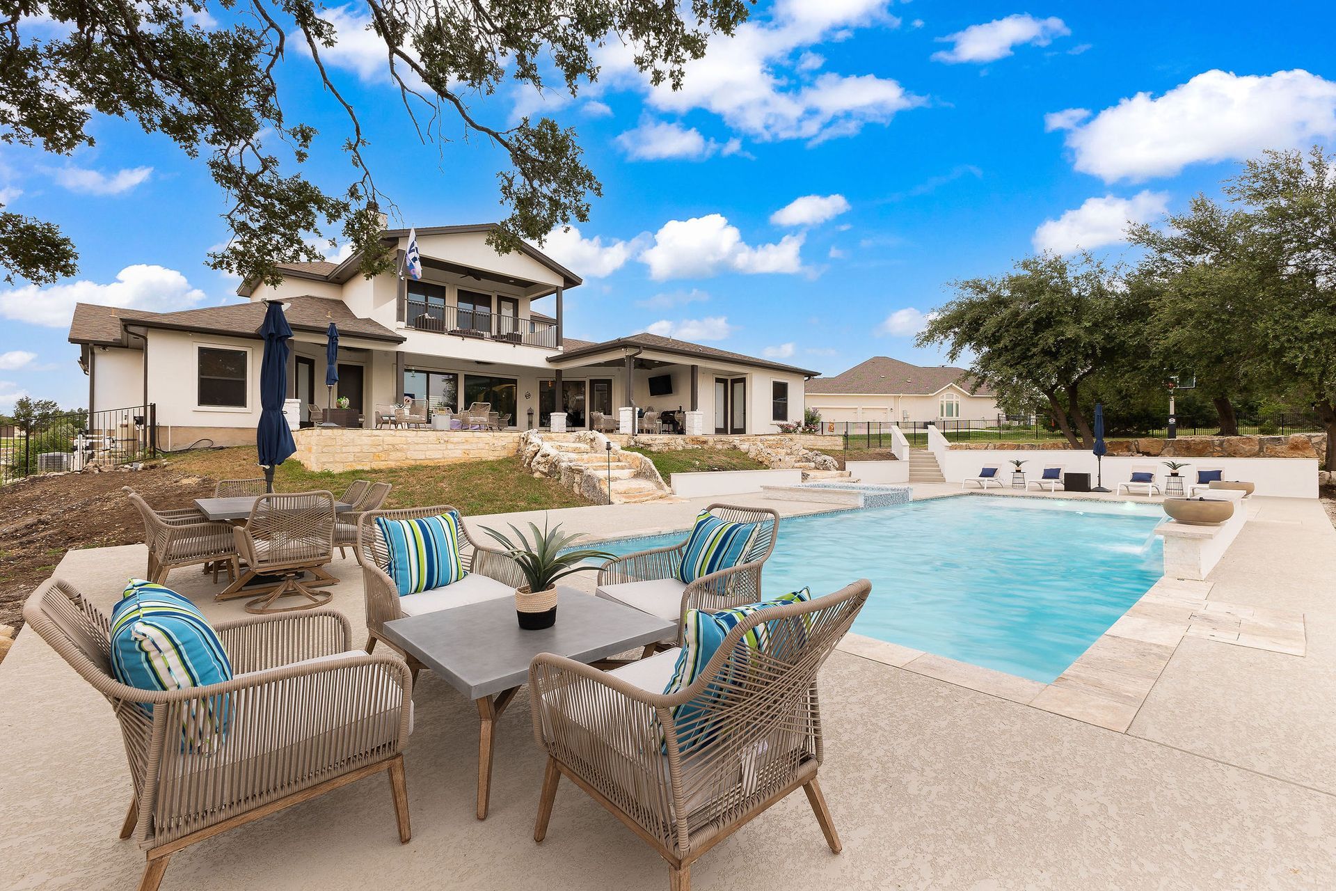 Backyard patio with wicker chairs, turquoise pool, and large modern home under a blue sky